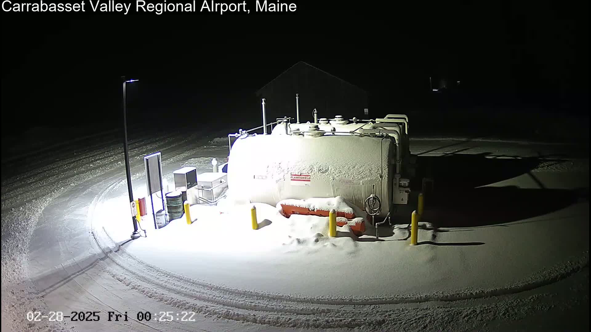 A snow-covered fuel tank sits in a snow-covered area at night, illuminated by a nearby lamppost.