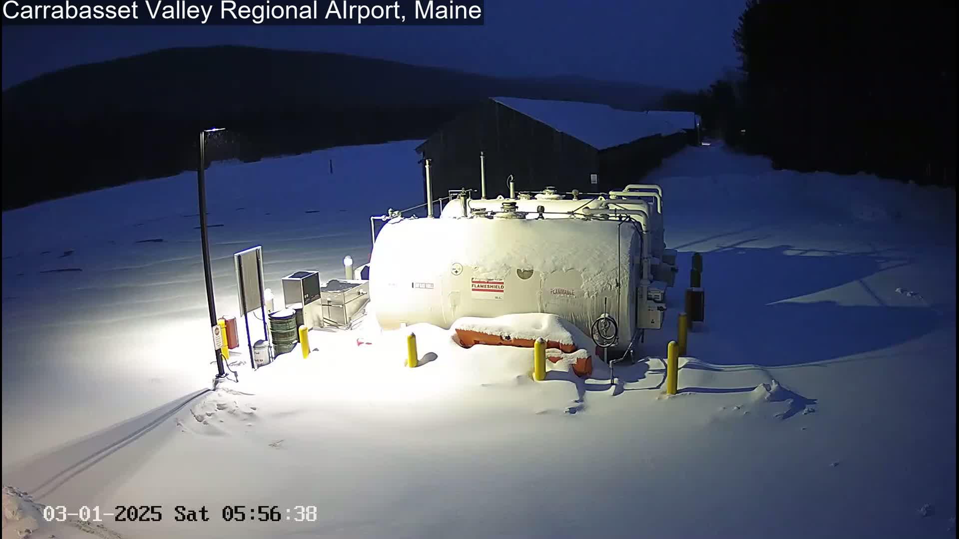 A large, snow-covered fuel tank sits in a snow-covered area at night.