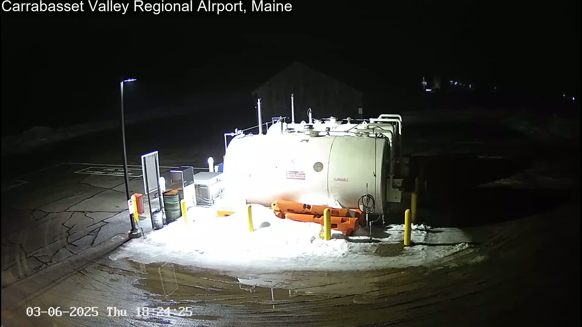 A large white flammable tank sits in a snow-covered, dimly lit outdoor area at night.