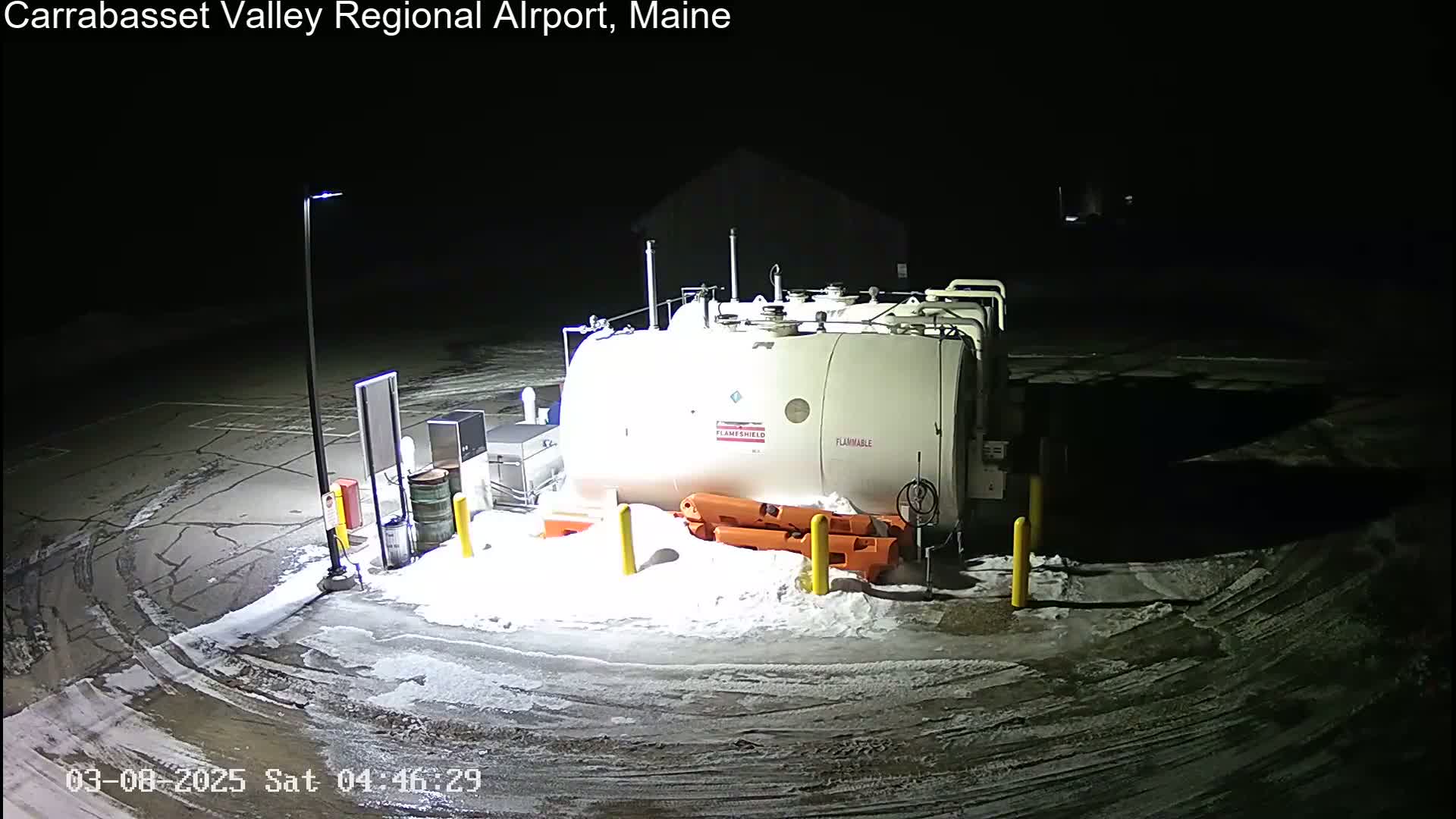 A large, white fuel tank sits in a snow-covered parking lot at night, illuminated by a single lamp.