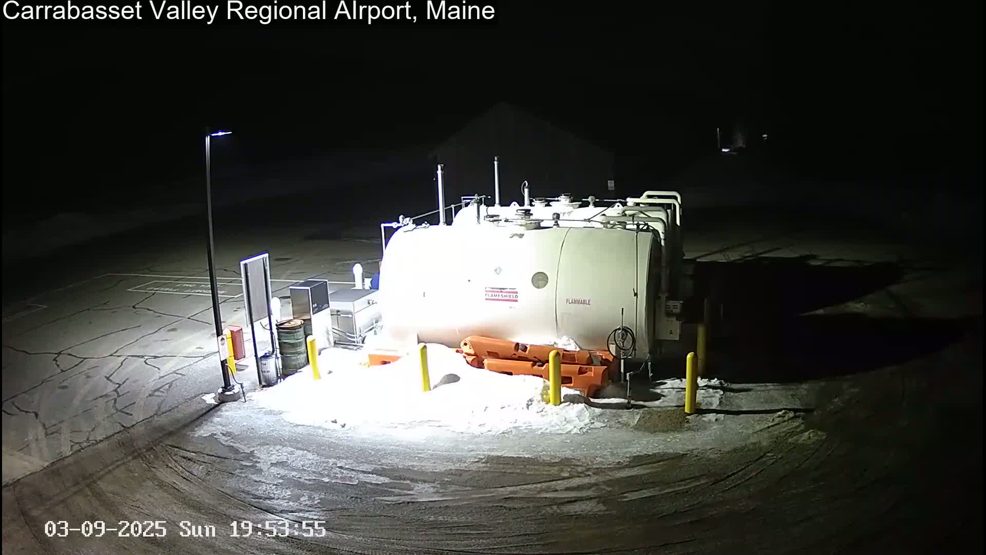A large, white fuel tank sits in a snow-covered, dimly lit outdoor area at night.