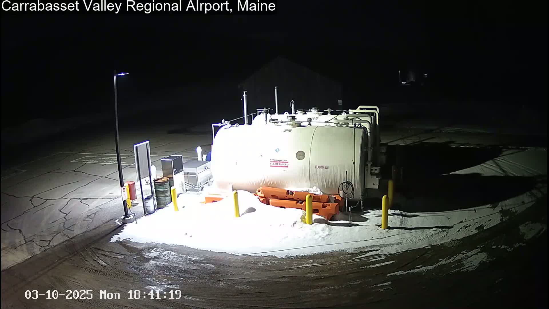 A large white fuel tank sits in a snow-covered area at night, illuminated by artificial light.