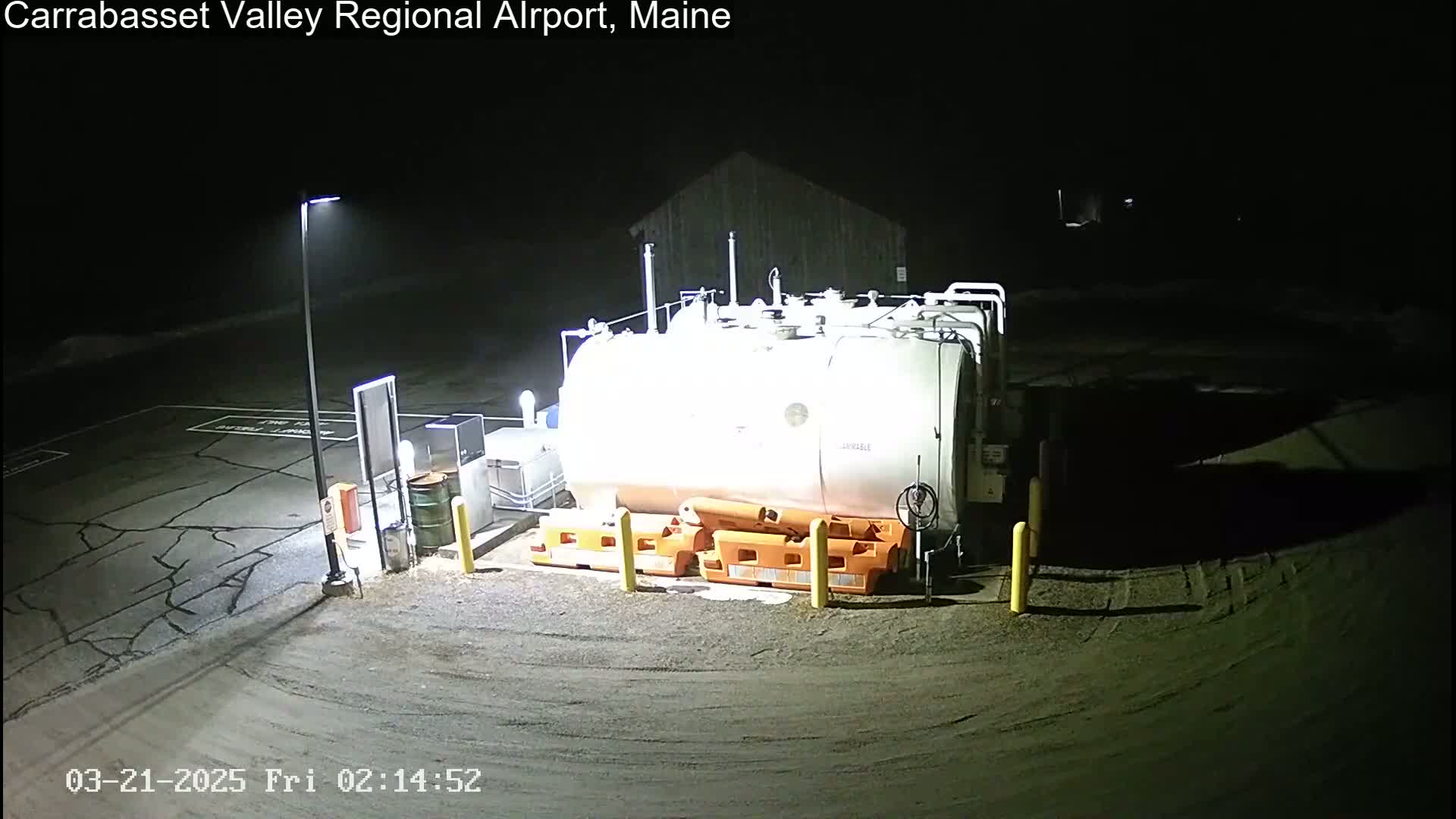 A large, light-colored fuel tank sits in a dark, empty lot at night, illuminated by a single lamppost.