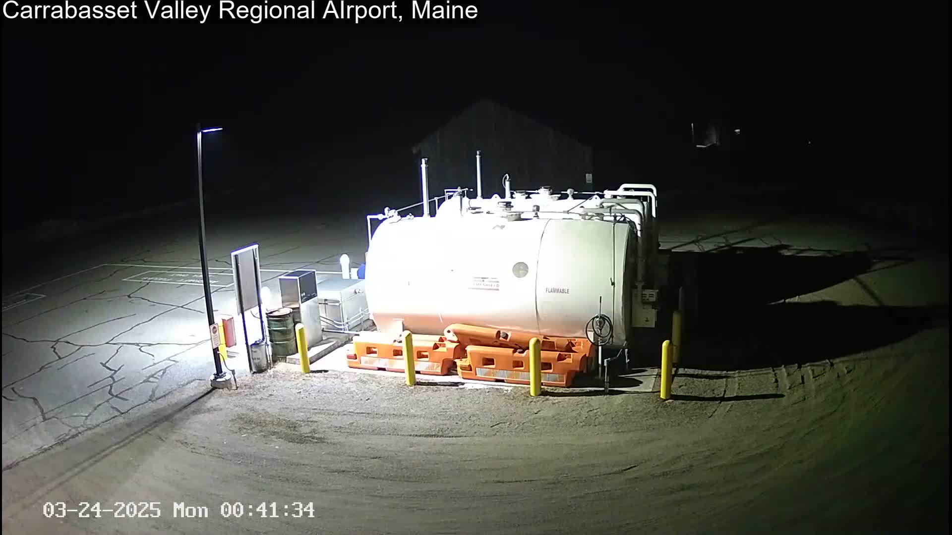 A large, white, cylindrical fuel tank sits in a dark, outdoor area under artificial light at night.