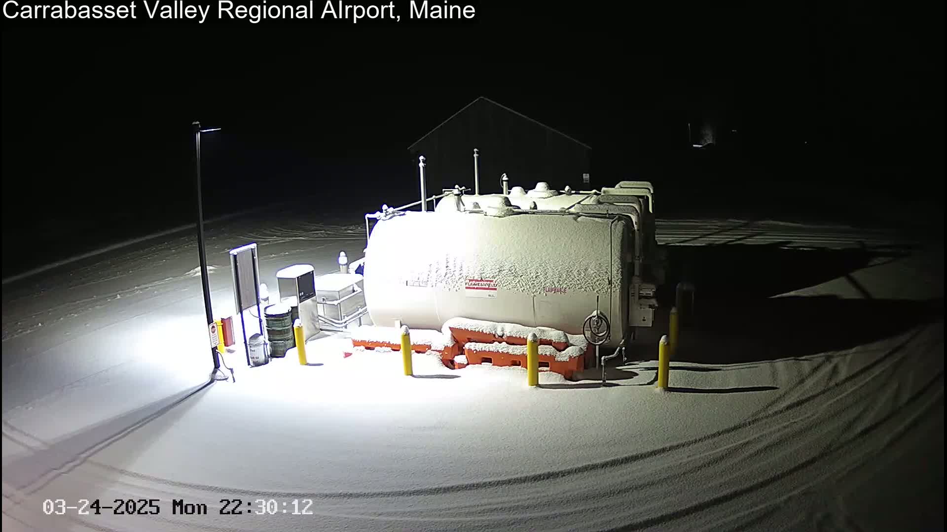 A snow-covered fuel tank sits in a snowy, dimly lit area at night.