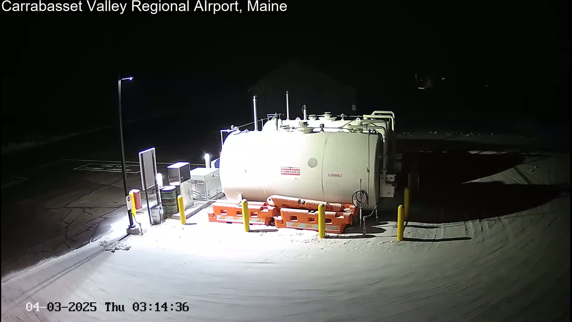A large, light-colored fuel tank sits in a snow-covered, dimly lit area at night.