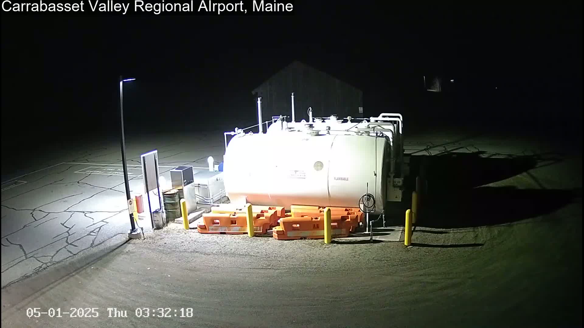 A large white fuel tank sits in a dark, paved lot at night, illuminated by a single lamppost.