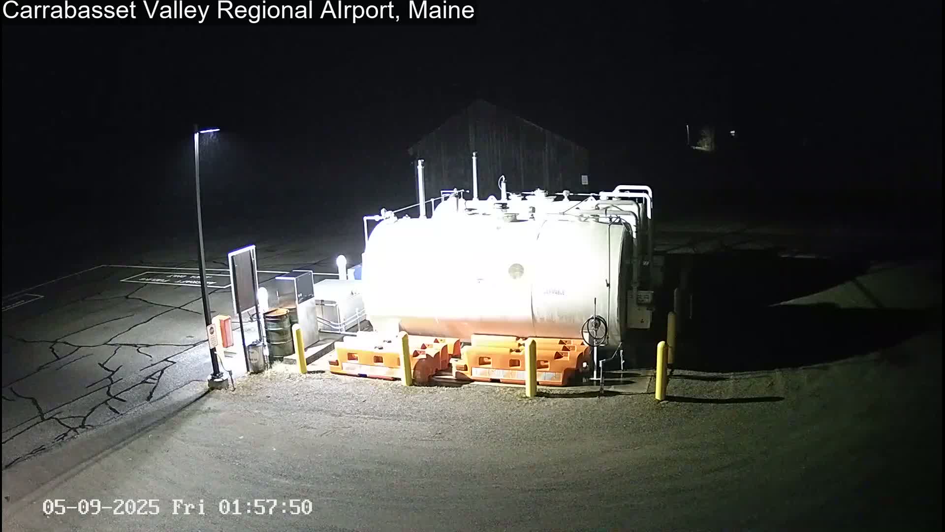 A large, cylindrical fuel tank sits in a dark, empty parking lot at night, illuminated by artificial light.