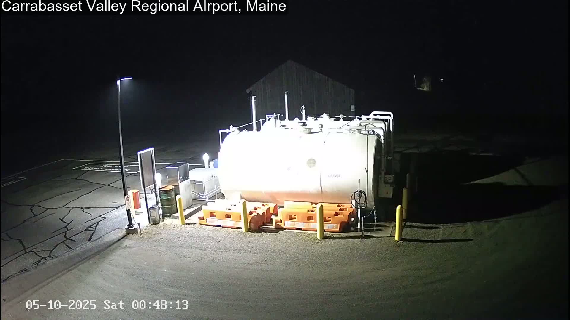 A large white fuel tank sits in a dark, outdoor, asphalt lot, illuminated by artificial light at night.
