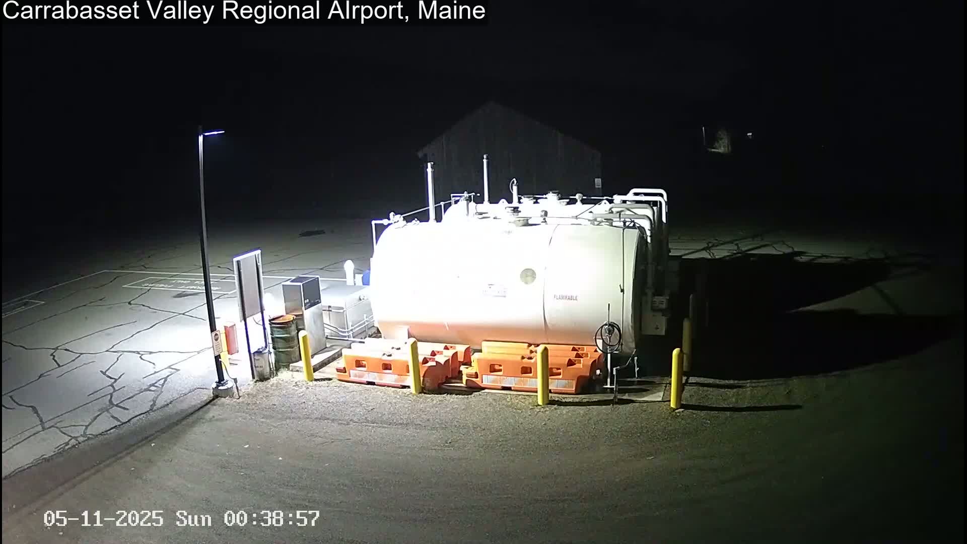 A large, white fuel tank sits in a dark, empty parking lot at night, illuminated by a single lamppost.