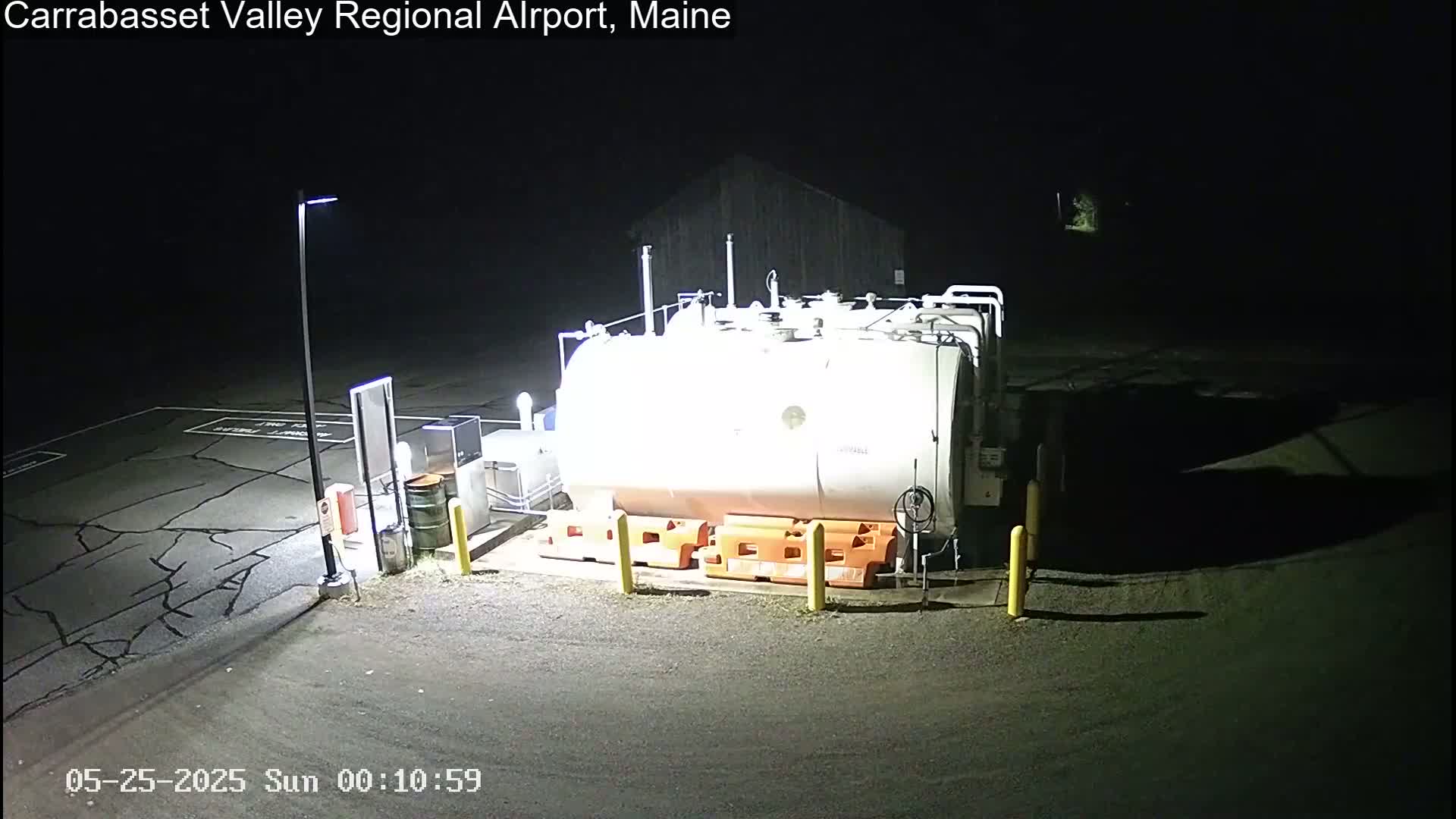 A large white tank sits in a dark, empty asphalt lot at night, illuminated by artificial light.