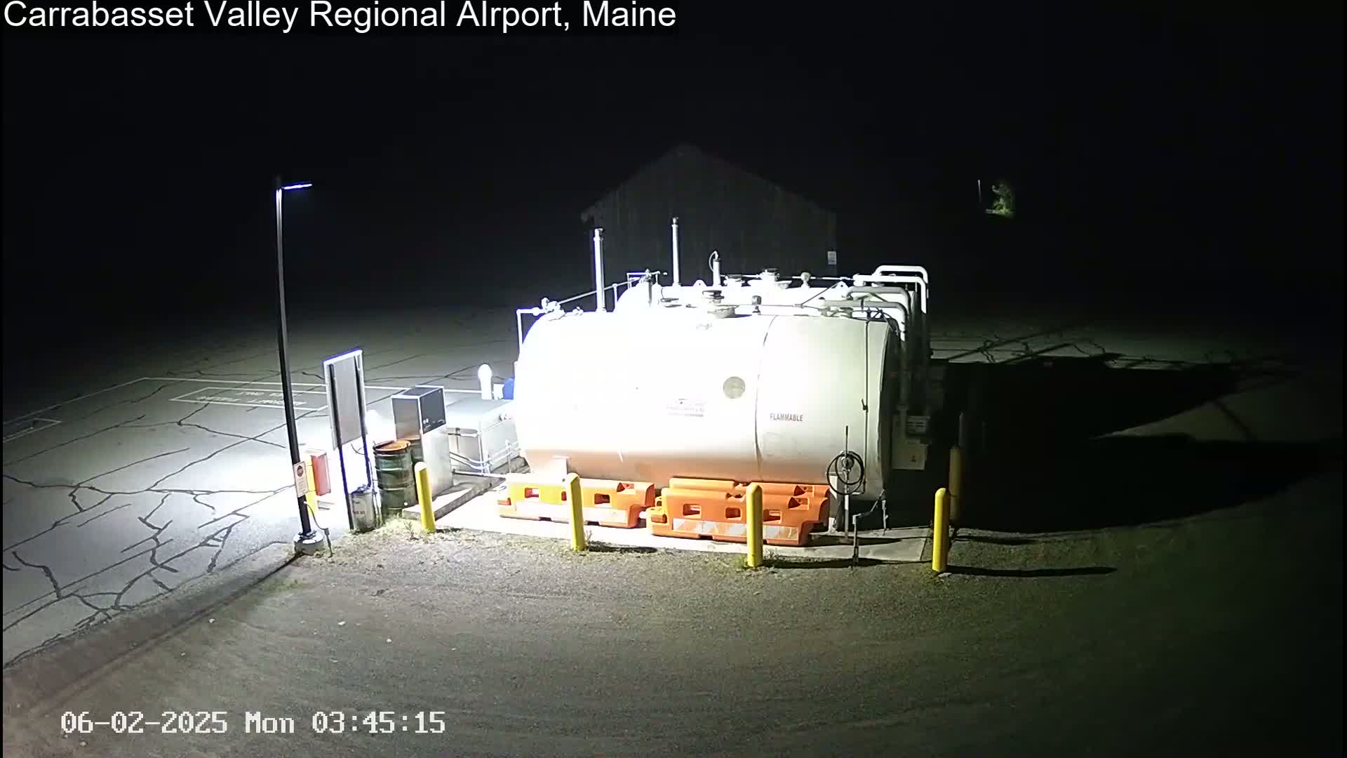 At night, a large white fuel tank sits in a dark asphalt lot, illuminated by a single lamppost.
