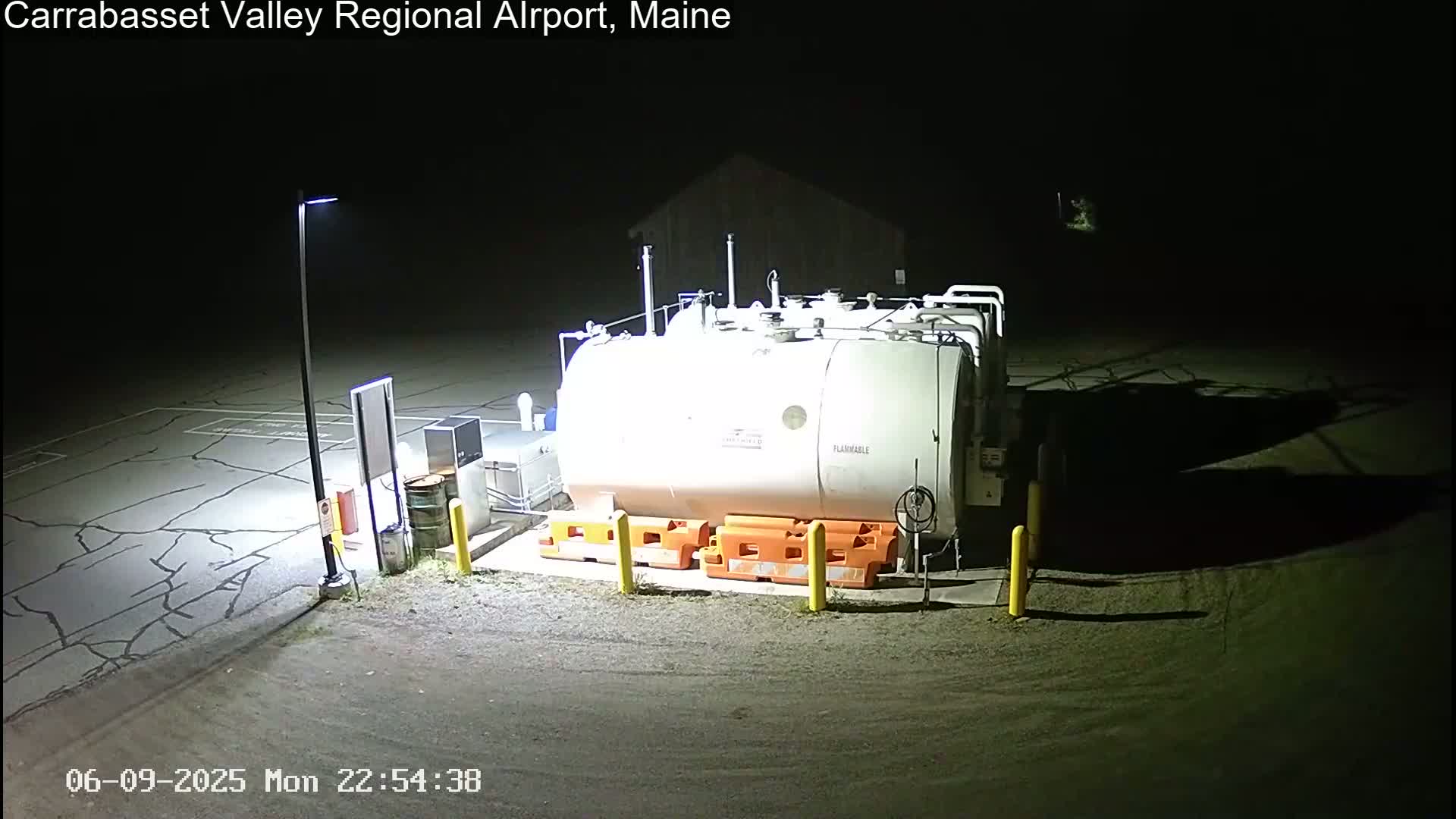 A large, white fuel tank sits in a dark, asphalt lot at night, illuminated by a single lamppost.