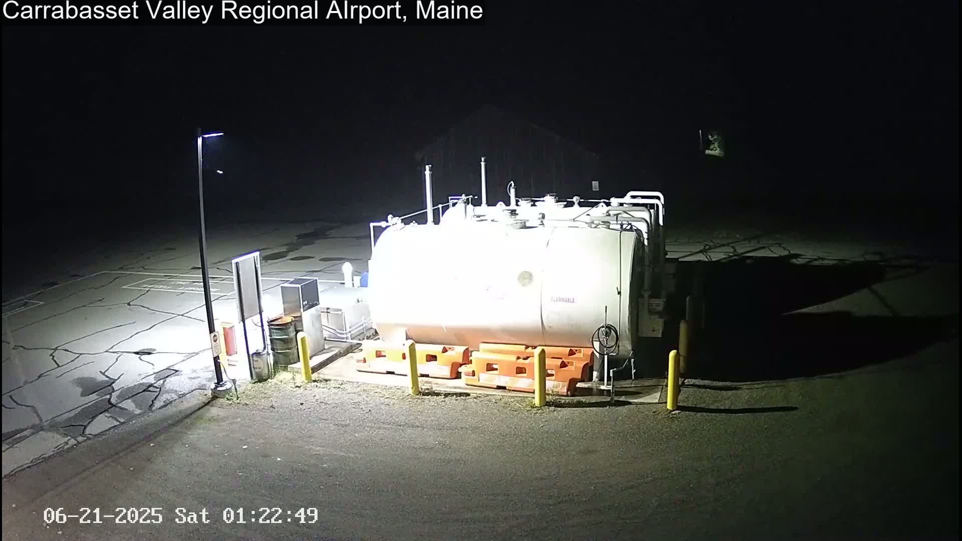 A large, light-colored fuel tank sits in a dark, empty lot at night, illuminated by artificial light.
