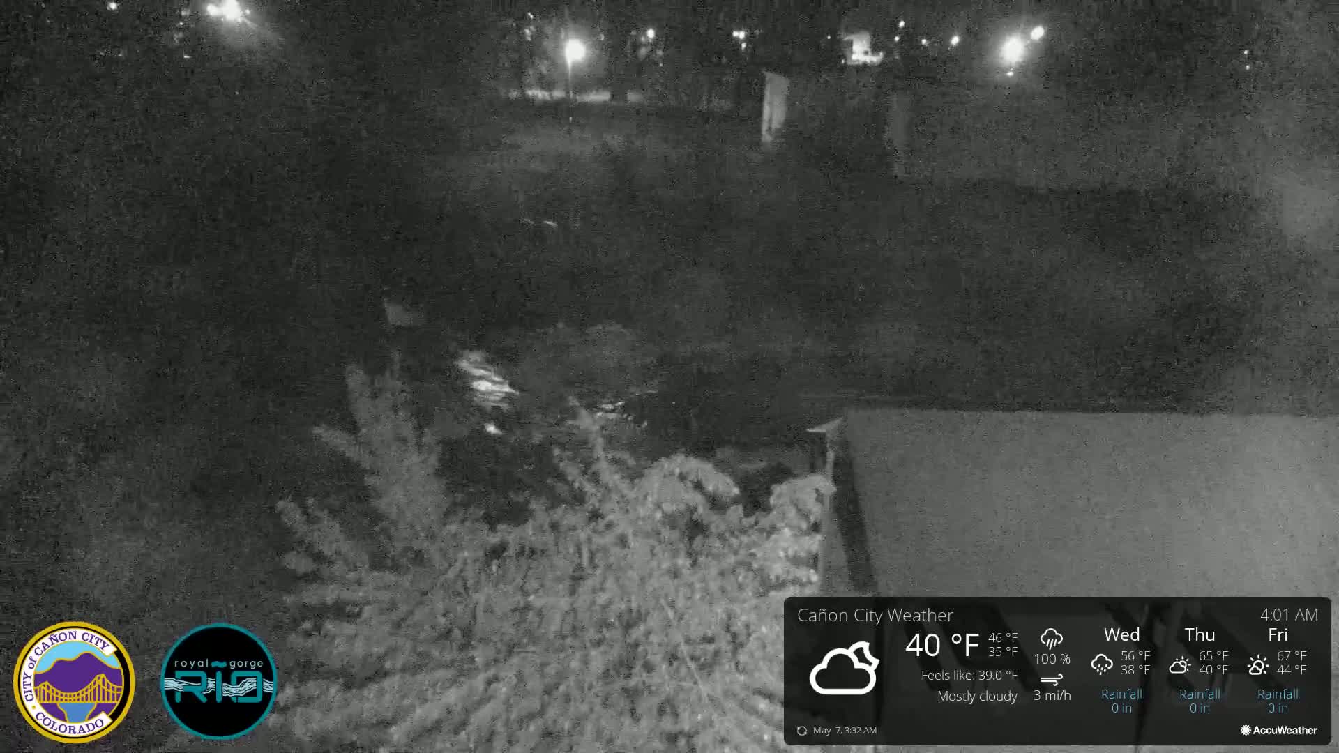 A nighttime, mostly cloudy scene shows dark vegetation near a body of water under dim artificial light.