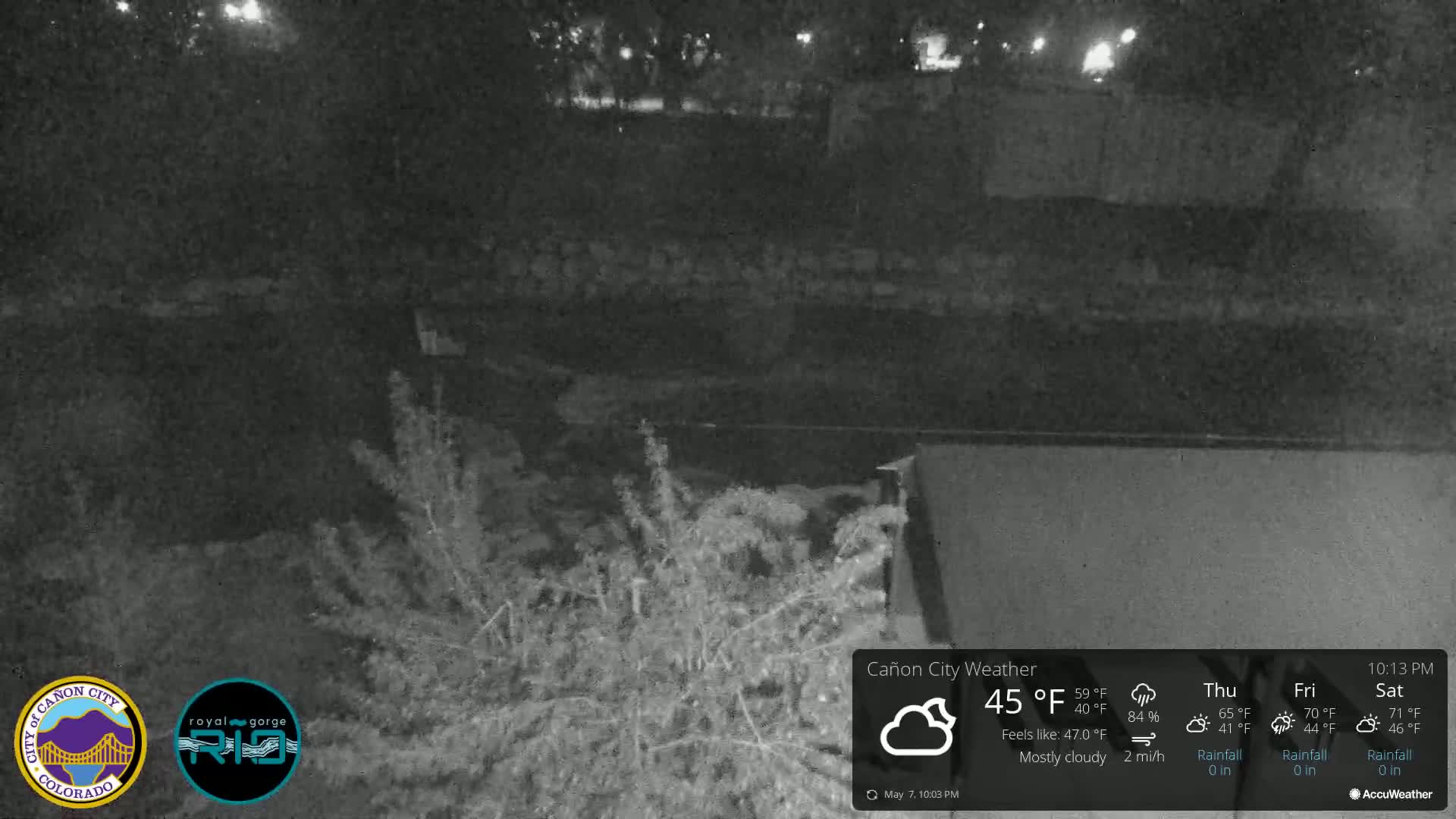 A nighttime, mostly cloudy scene shows a dark body of water next to shrubbery under dim lighting.