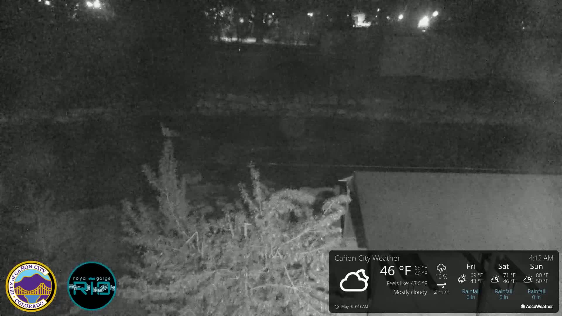 A nighttime, mostly cloudy scene shows a dark body of water and vegetation near a wall.