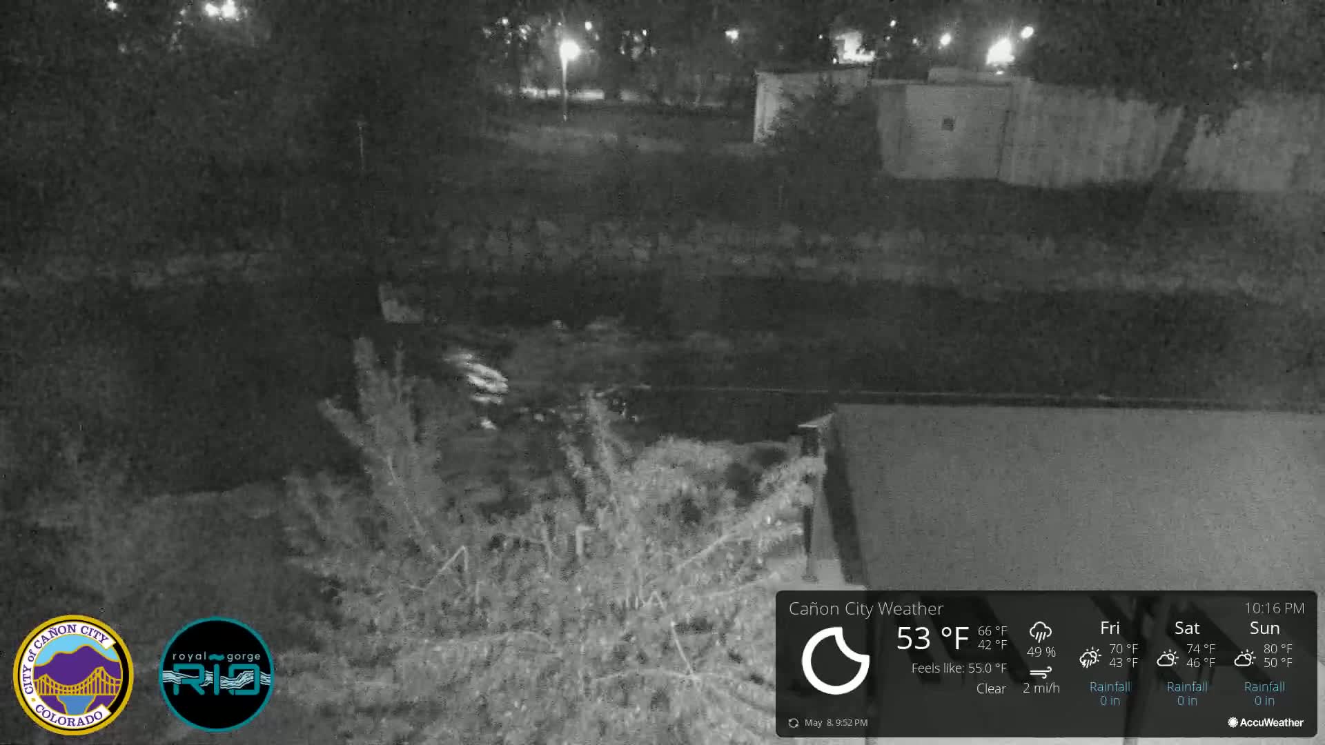 A nighttime, clear view of a dark body of water, partially obscured by vegetation, with a building visible in the bottom right corner.