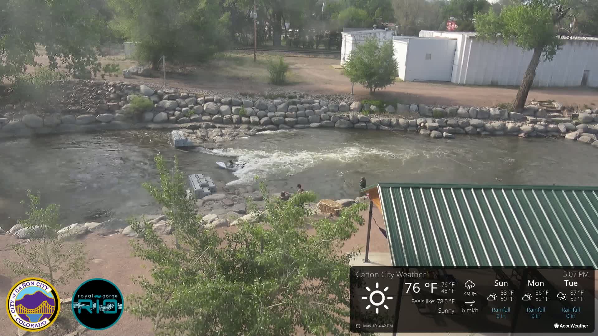 A rocky riverbank with a person kayaking in a sunny, mild-weather setting.