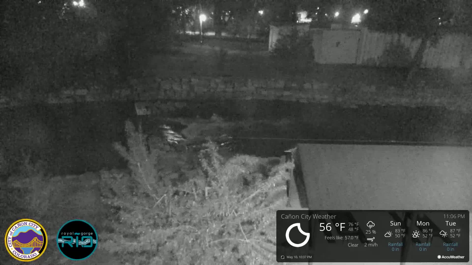 A nighttime, clear view of a dark, flowing body of water next to a low wall and vegetation.