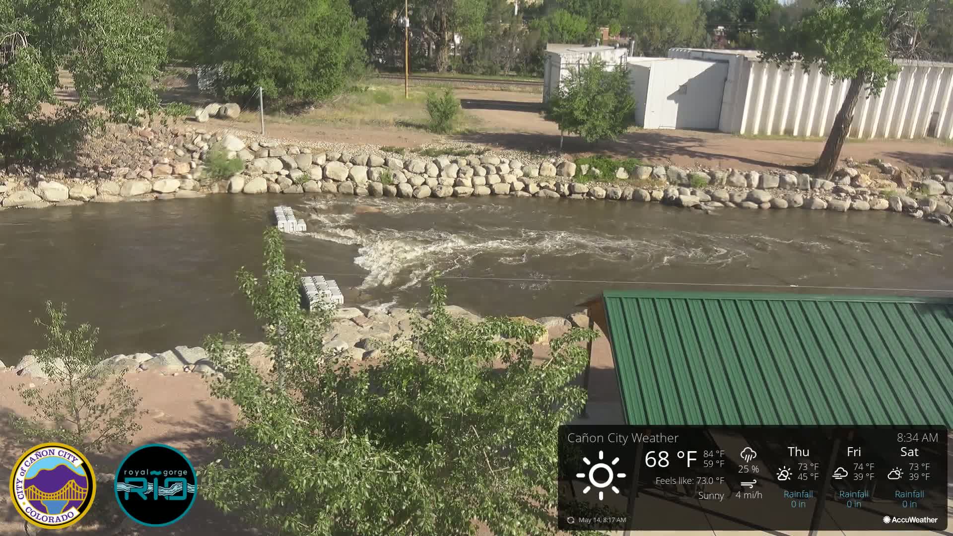 A fast-flowing river with rocky banks and several floating structures under a sunny sky.