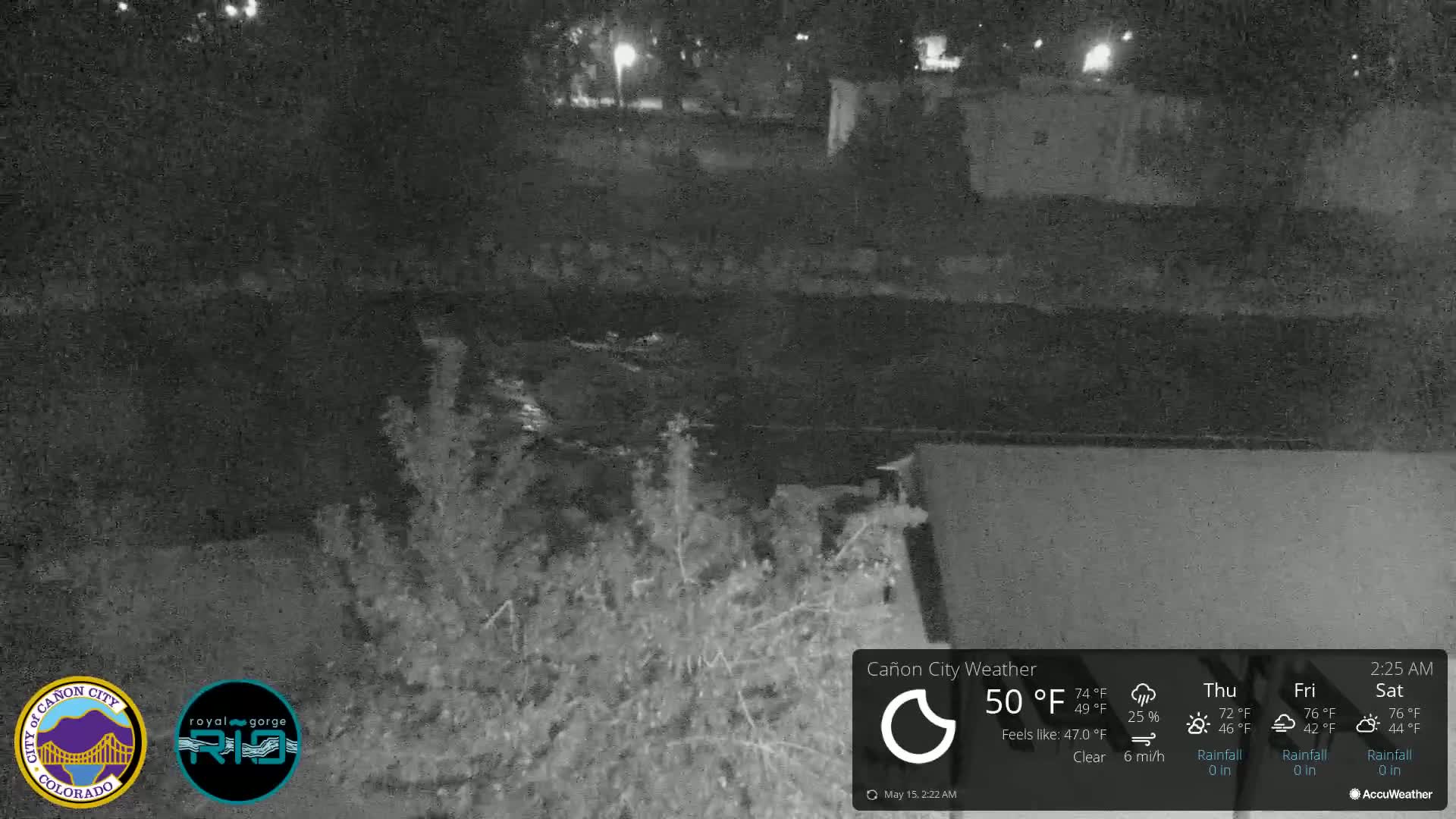 A nighttime, clear view of a dark river flowing under a bridge, with bushes and vegetation visible along the riverbank.