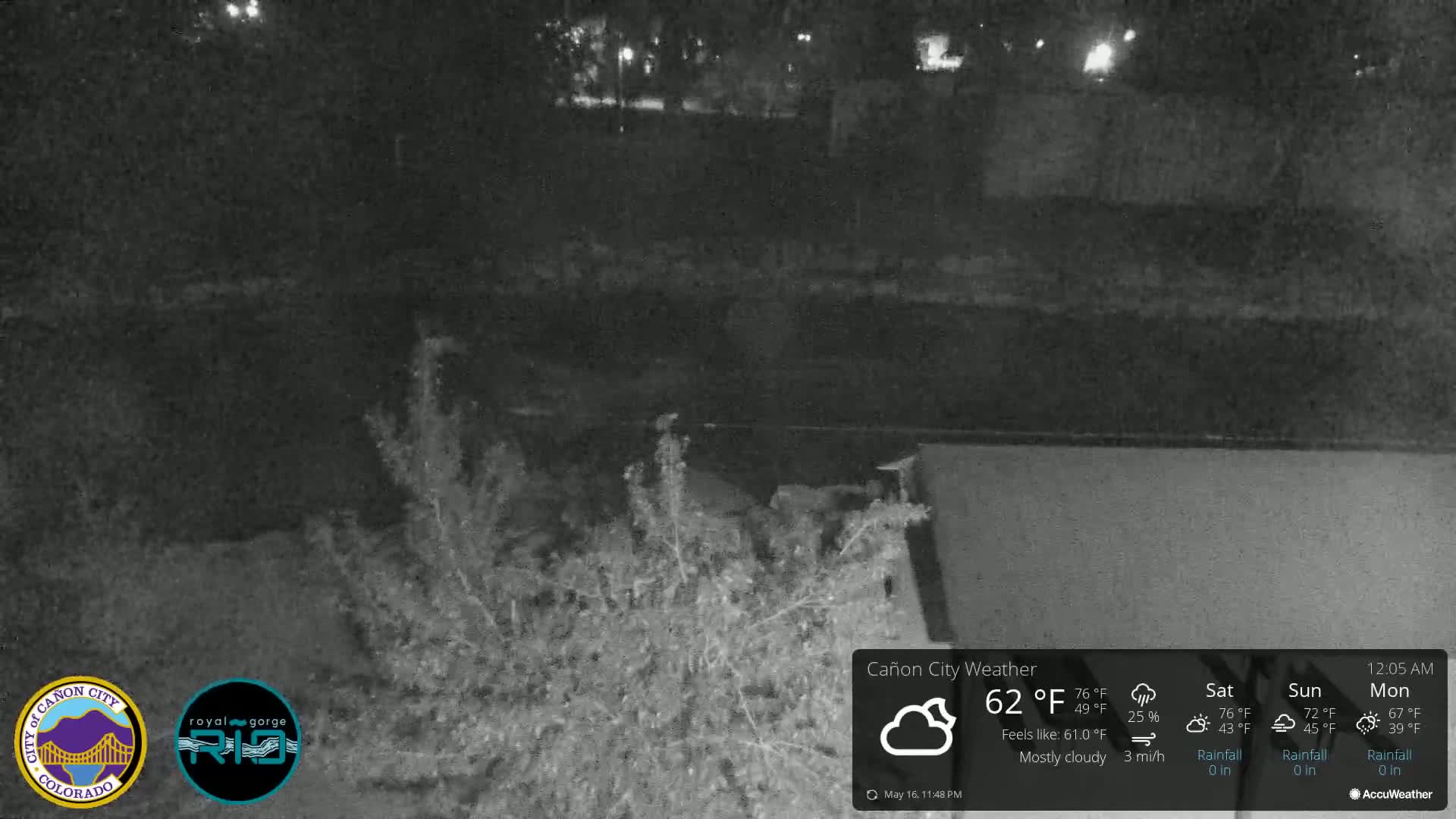 A nighttime, mostly cloudy scene shows a dark body of water, some low vegetation, and a portion of a dark structure.