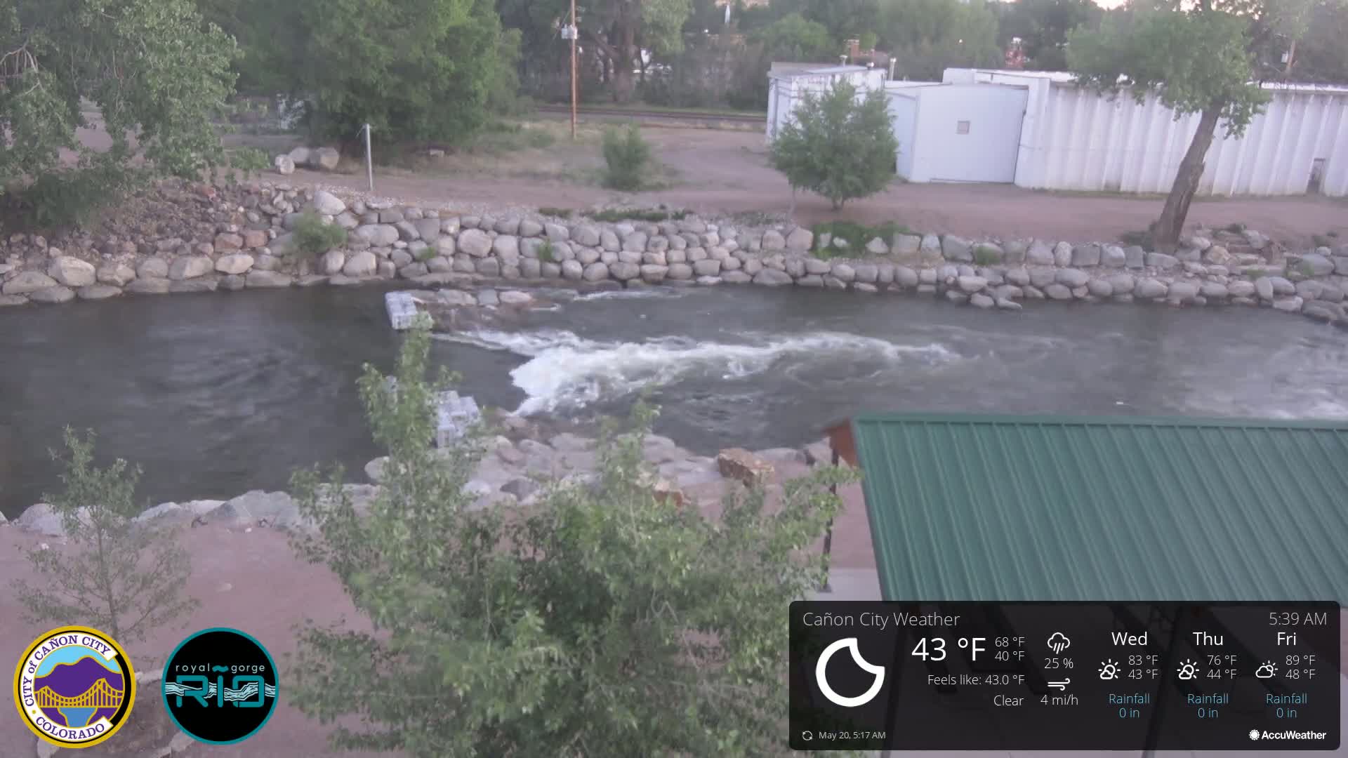 A river flows under a mostly clear sky, its water churning slightly over rocks and a man-made structure.