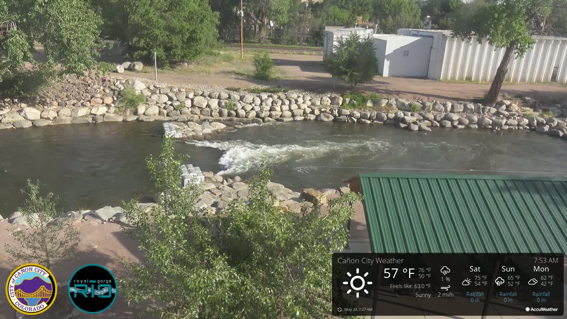A sunny day reveals a rocky riverbank with a fast-flowing section of water partially dammed by concrete blocks.