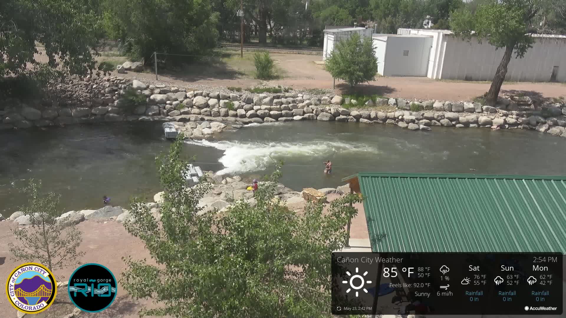 A sunny view of a river with people swimming and playing in the water, surrounded by rocks and vegetation.