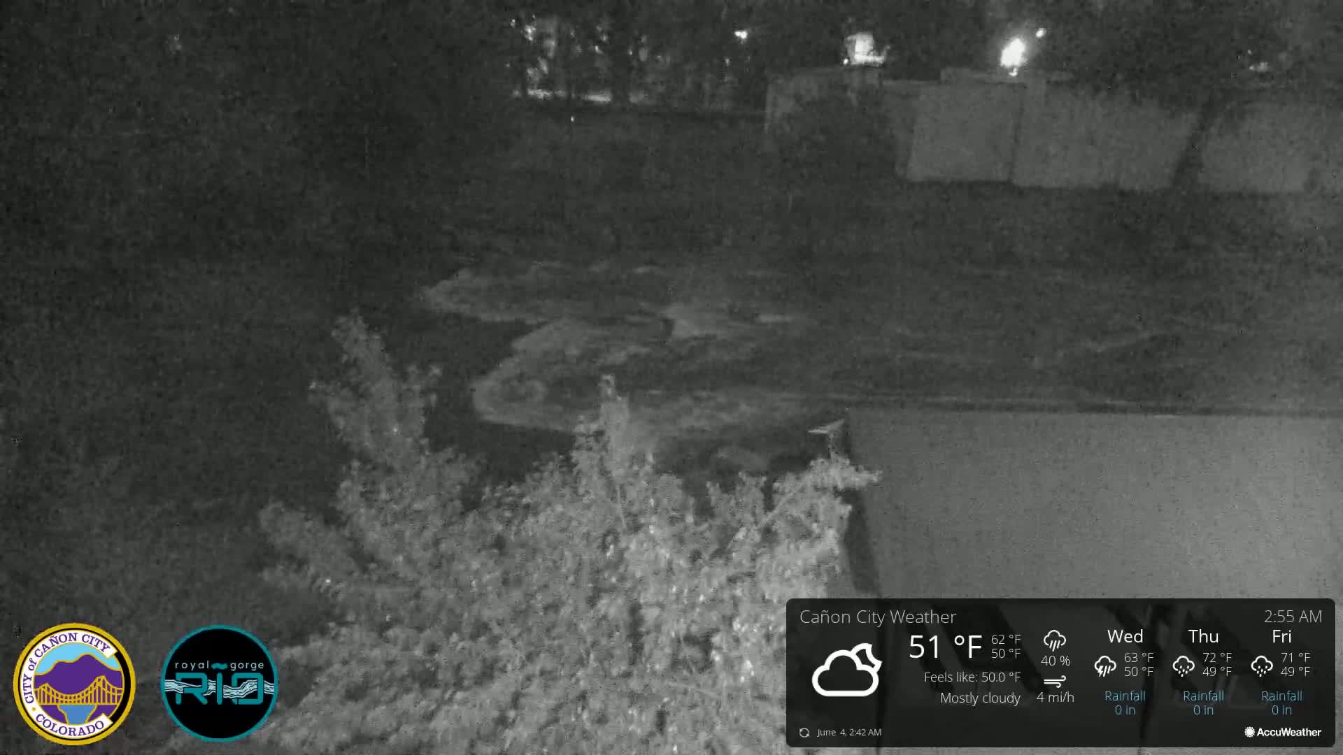 A nighttime, mostly cloudy scene shows a dark, water-filled area, possibly a stream or drainage ditch, surrounded by dark vegetation.