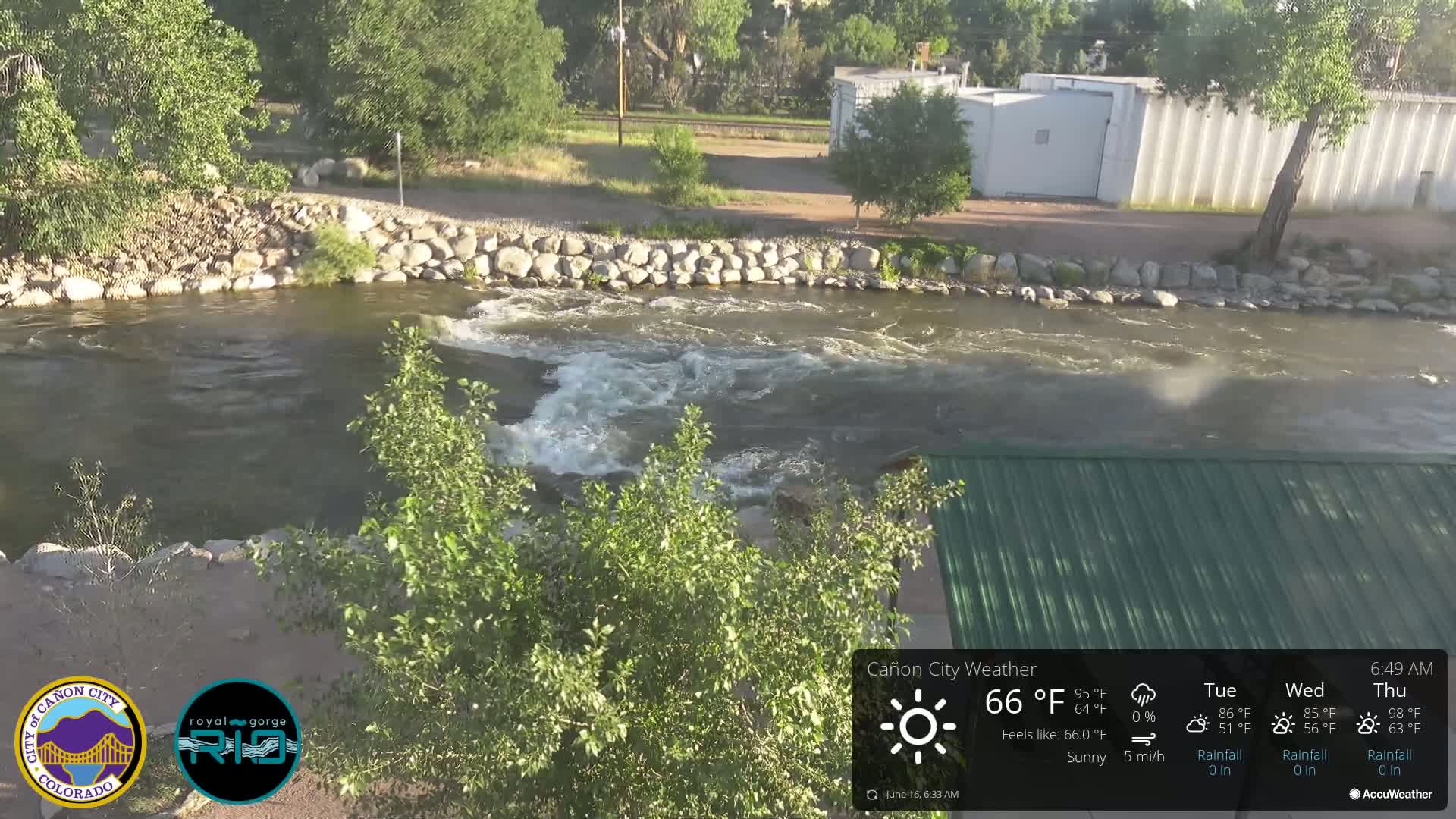 A partly sunny view of a rocky riverbank with a swiftly flowing river under a partly sunny sky.