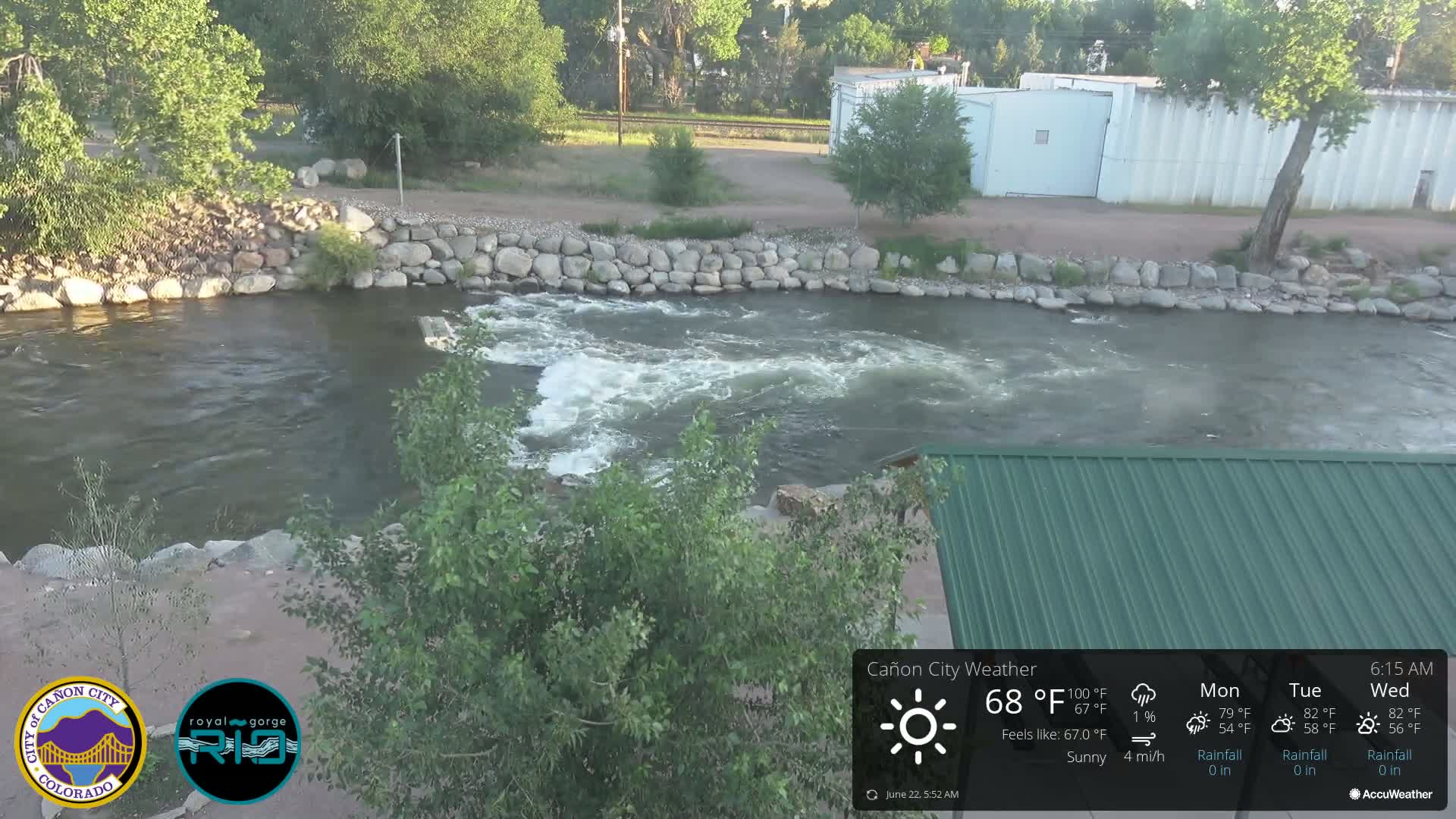 A partly sunny view of a river flowing over a rock embankment, with green vegetation along the banks.