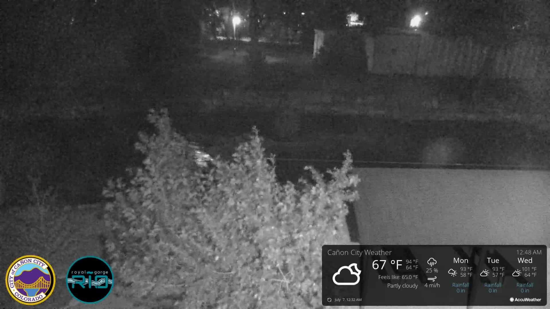 A nighttime, partly cloudy scene shows a dark body of water with shrubbery in the foreground.