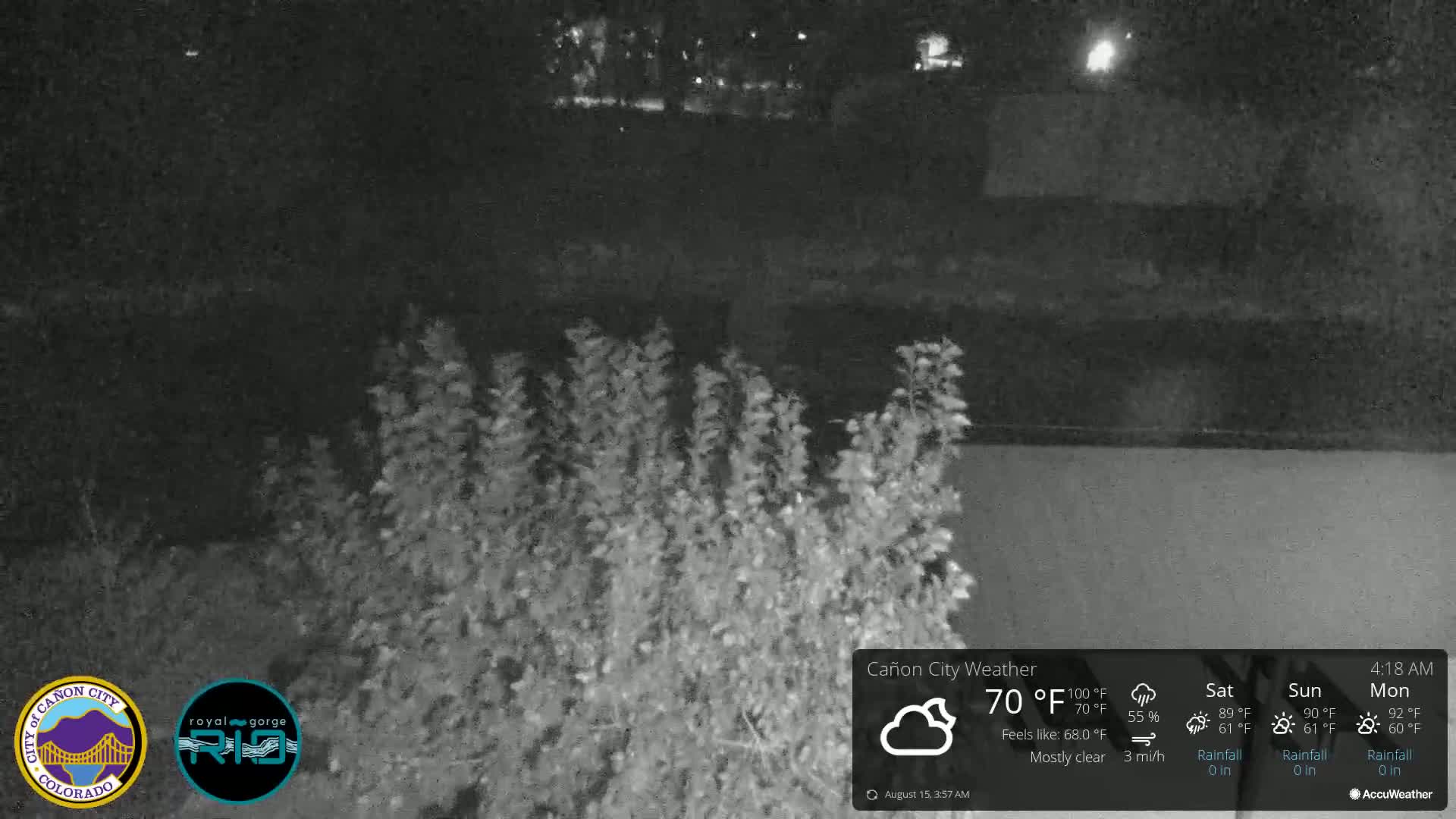 A nighttime, mostly cloudy scene shows dark shrubs in the foreground with a dark body of water and more dark land in the background.