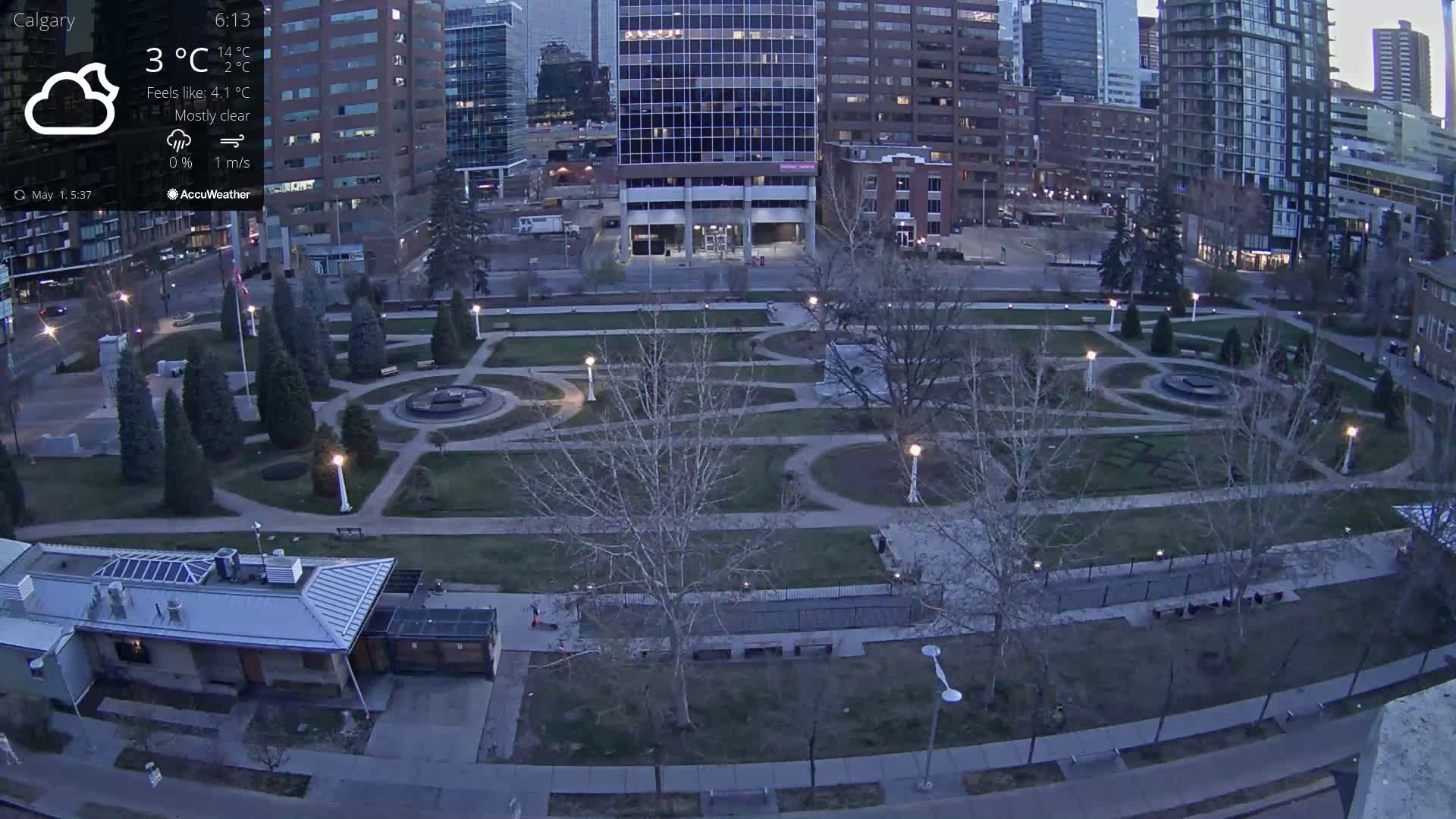 A mostly clear evening view of a city park with geometrically-designed landscaping, surrounded by tall buildings.