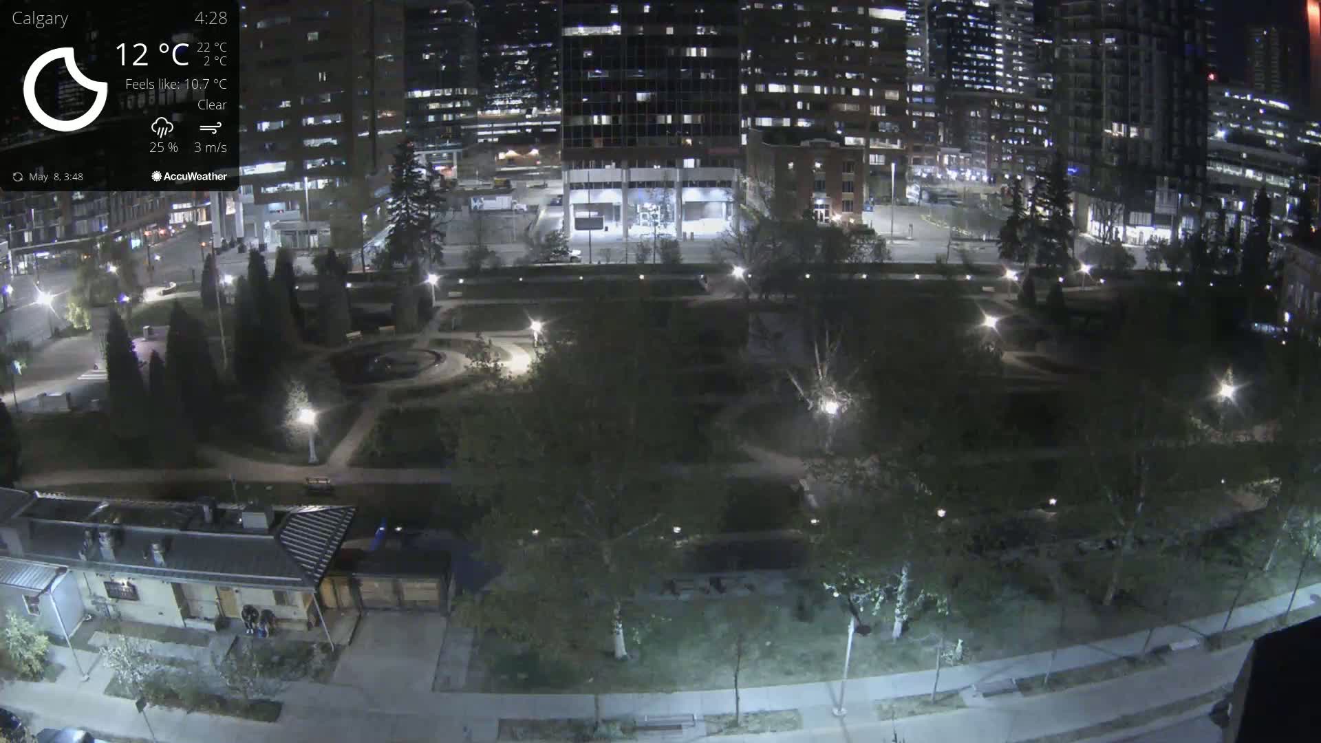 A nighttime aerial view of a city park with surrounding buildings, illuminated by lights under clear skies.