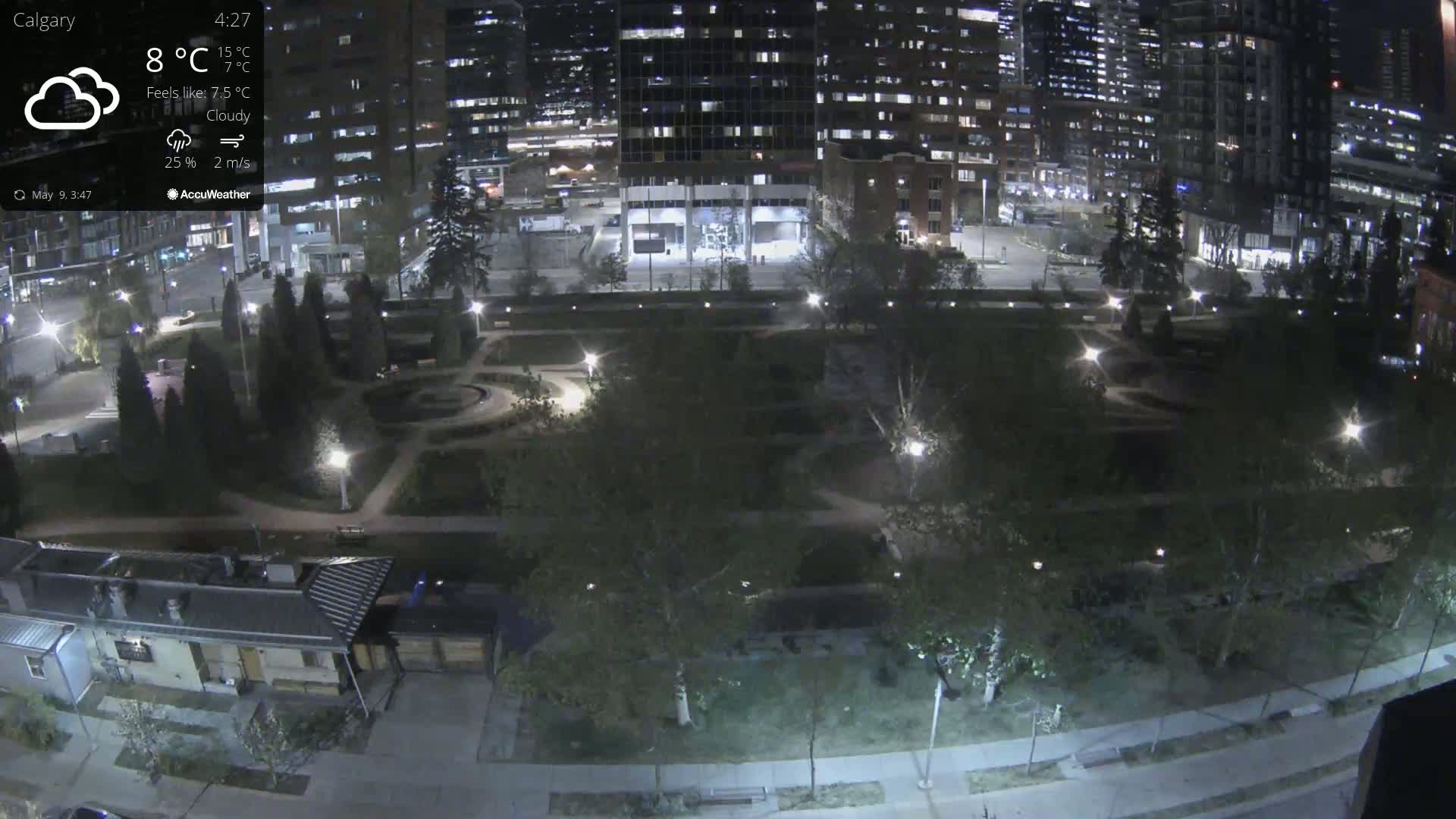A nighttime view of a city park, illuminated by streetlights under cloudy skies.