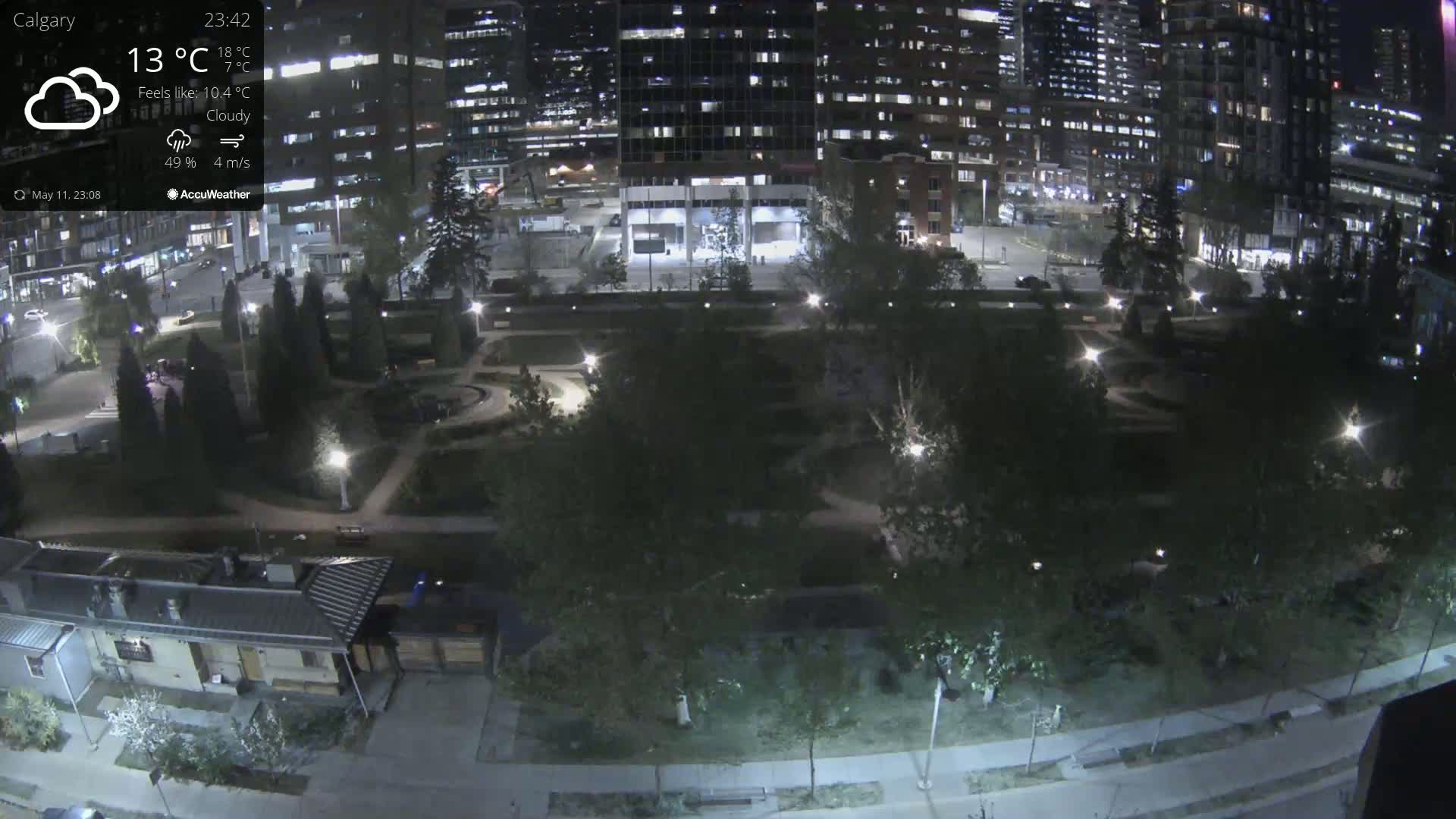 A nighttime, cloudy view of a city park surrounded by illuminated buildings and trees.