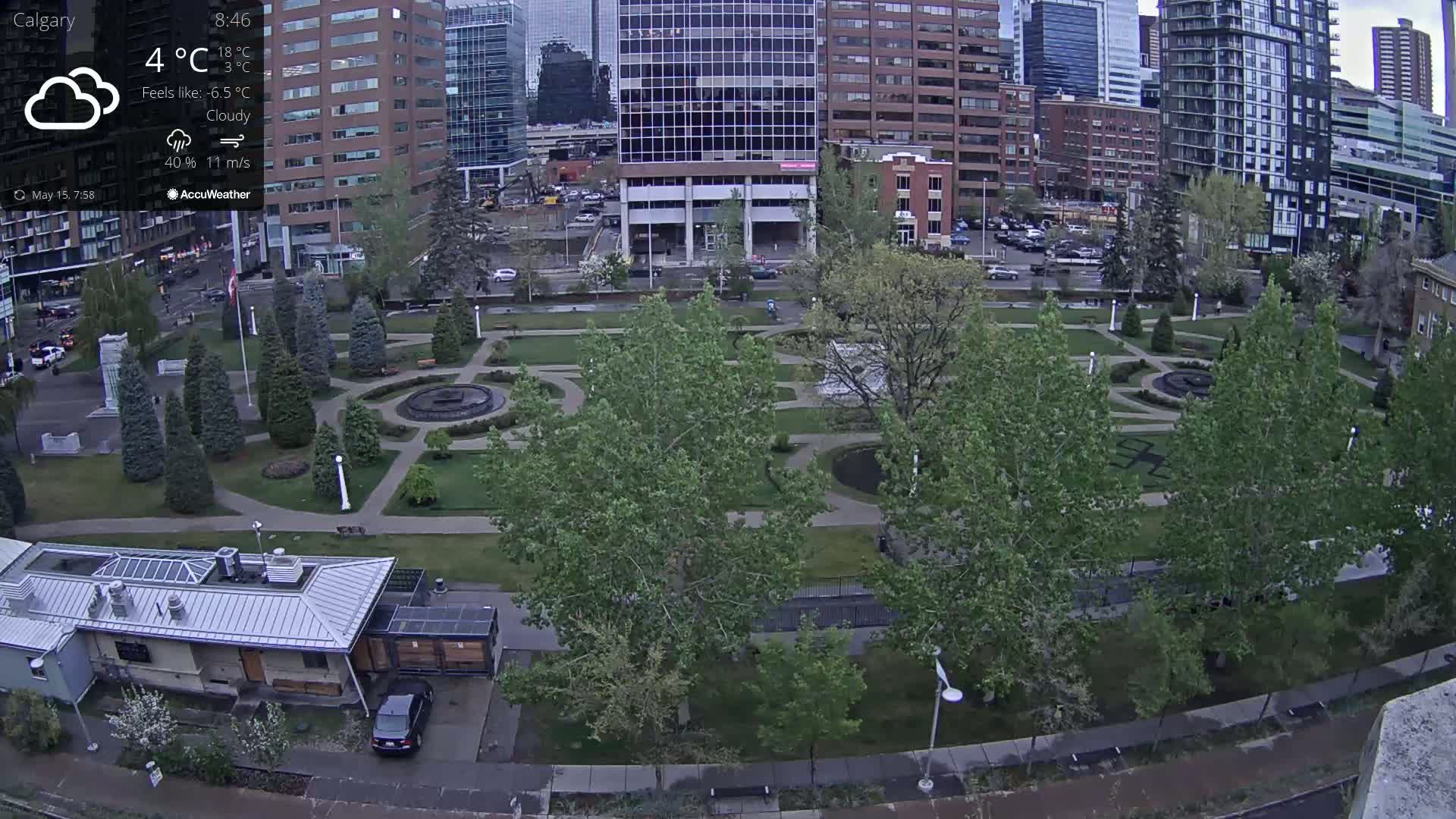A city park with a fountain and landscaping is visible beneath cloudy skies and a 4°C temperature, surrounded by buildings.
