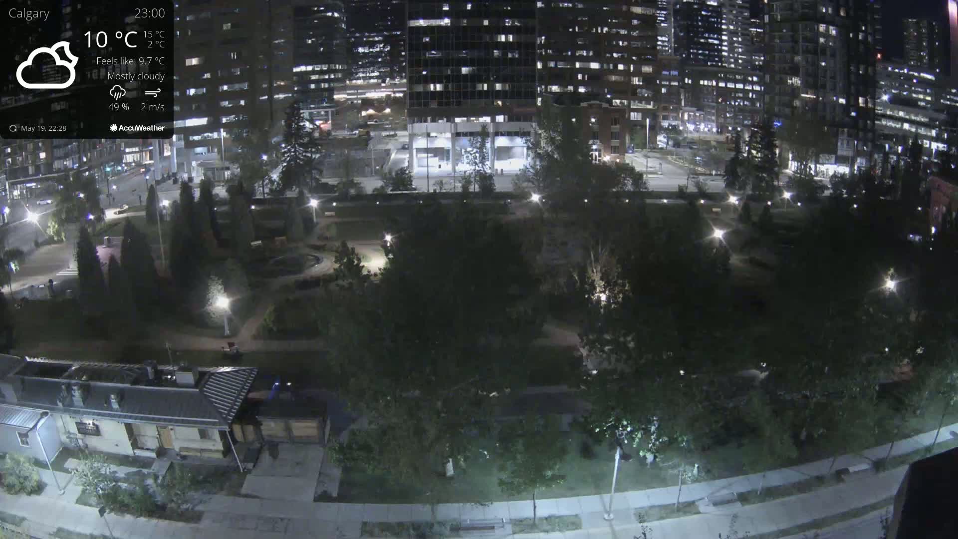 A nighttime, mostly cloudy view of a city park with surrounding buildings and streetlights under a 10°C temperature.