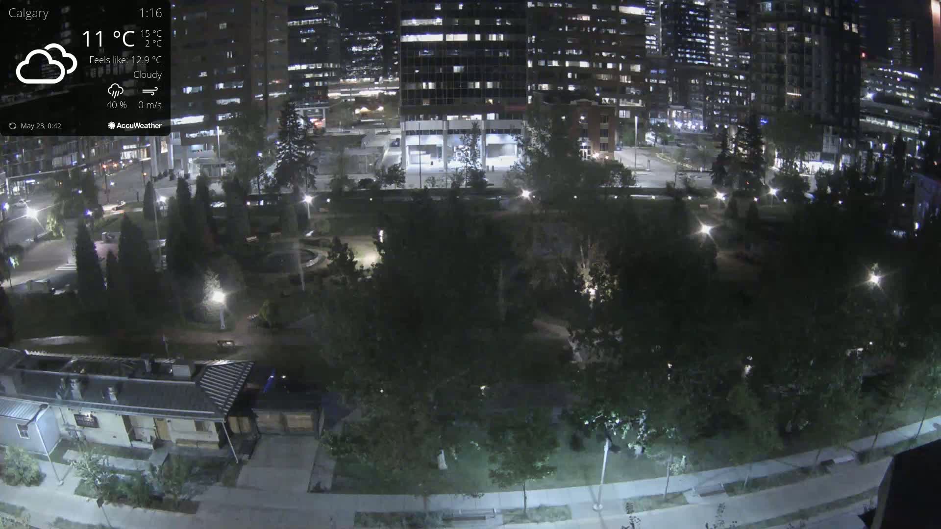 A nighttime, cloudy view of a city park surrounded by illuminated buildings.