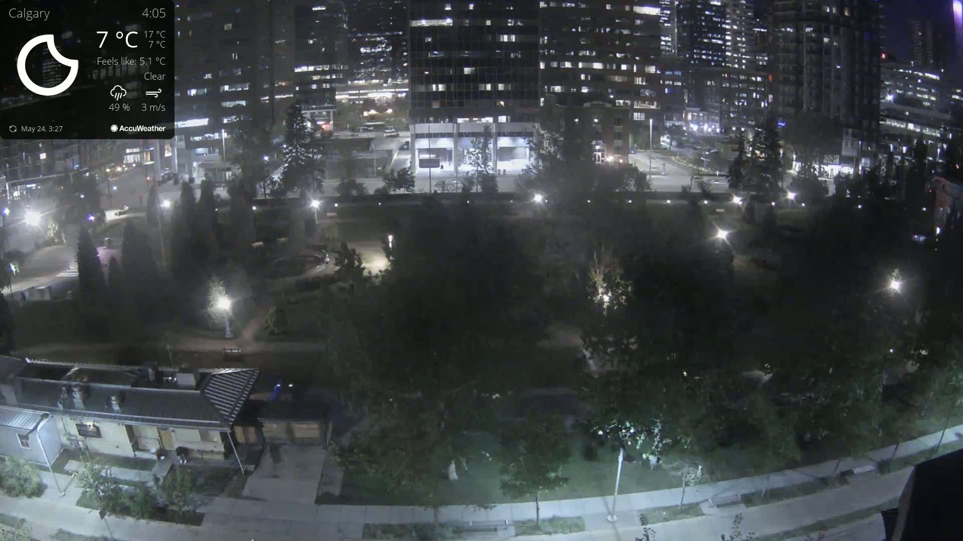 A nighttime, clear view of a park with city buildings in the background, illuminated by streetlights.