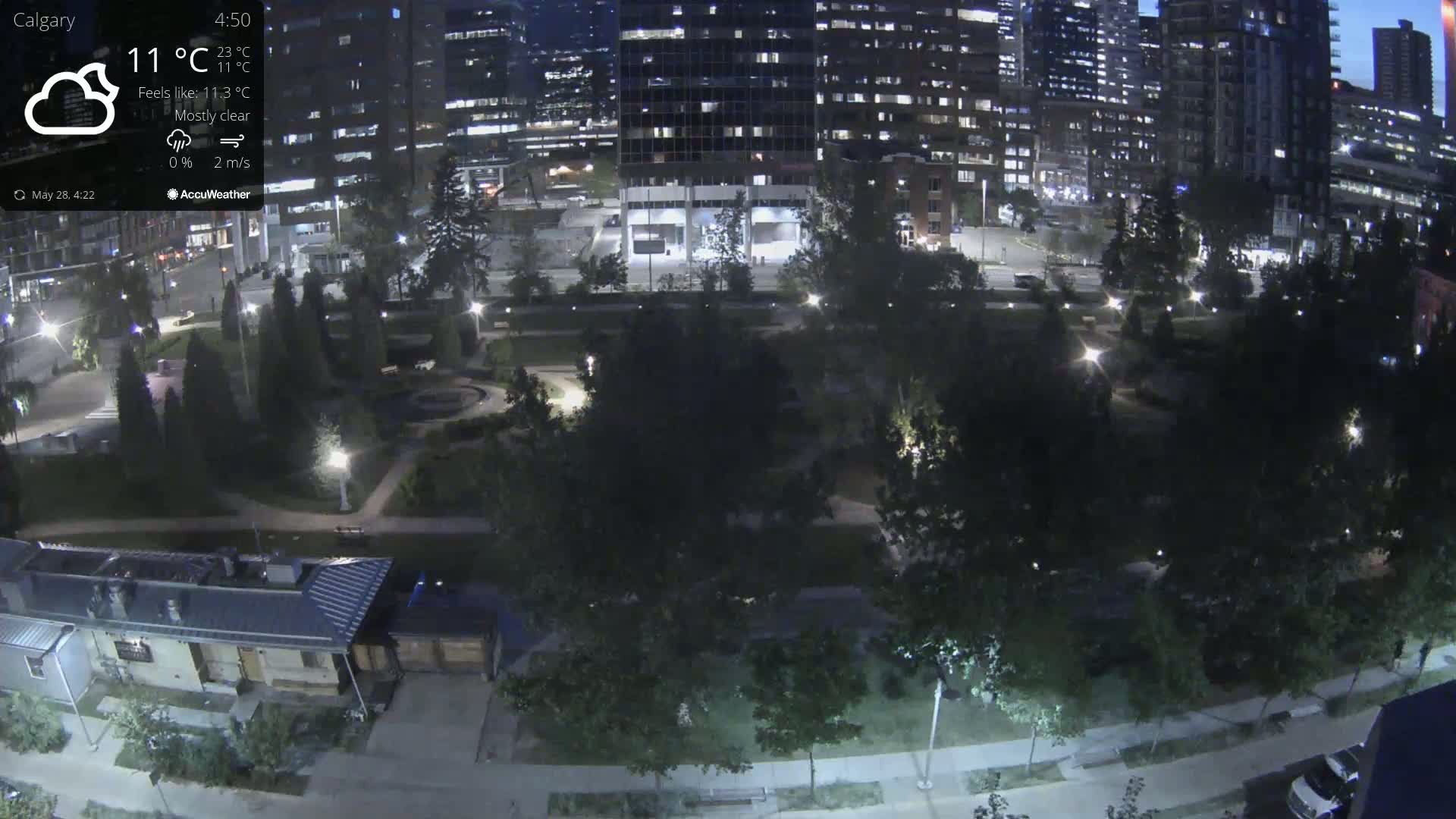 A nighttime aerial view of a city park bordered by illuminated buildings under mostly clear skies.