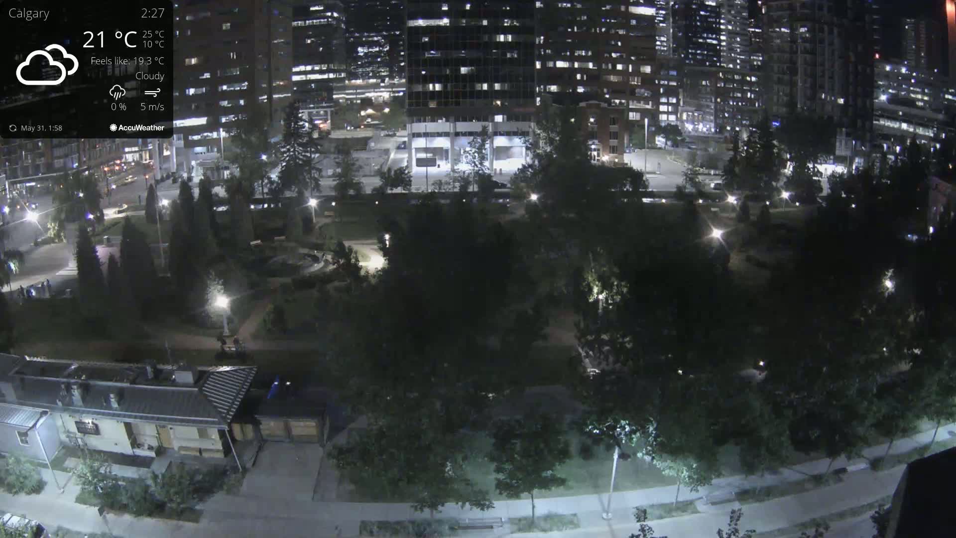 A nighttime, cloudy view of a city park surrounded by tall buildings.