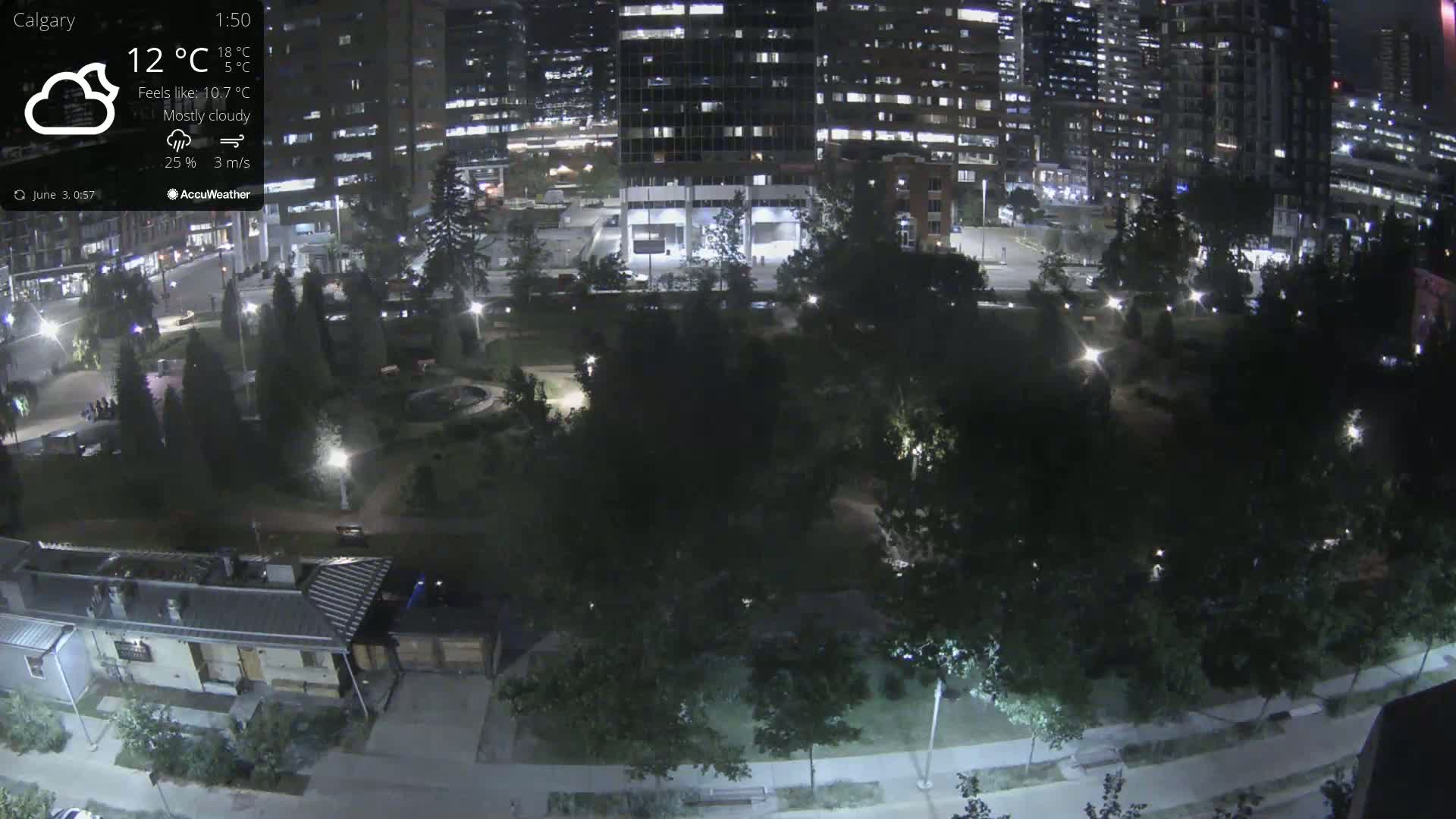 A mostly cloudy nighttime view of a park surrounded by city buildings, illuminated by streetlights.