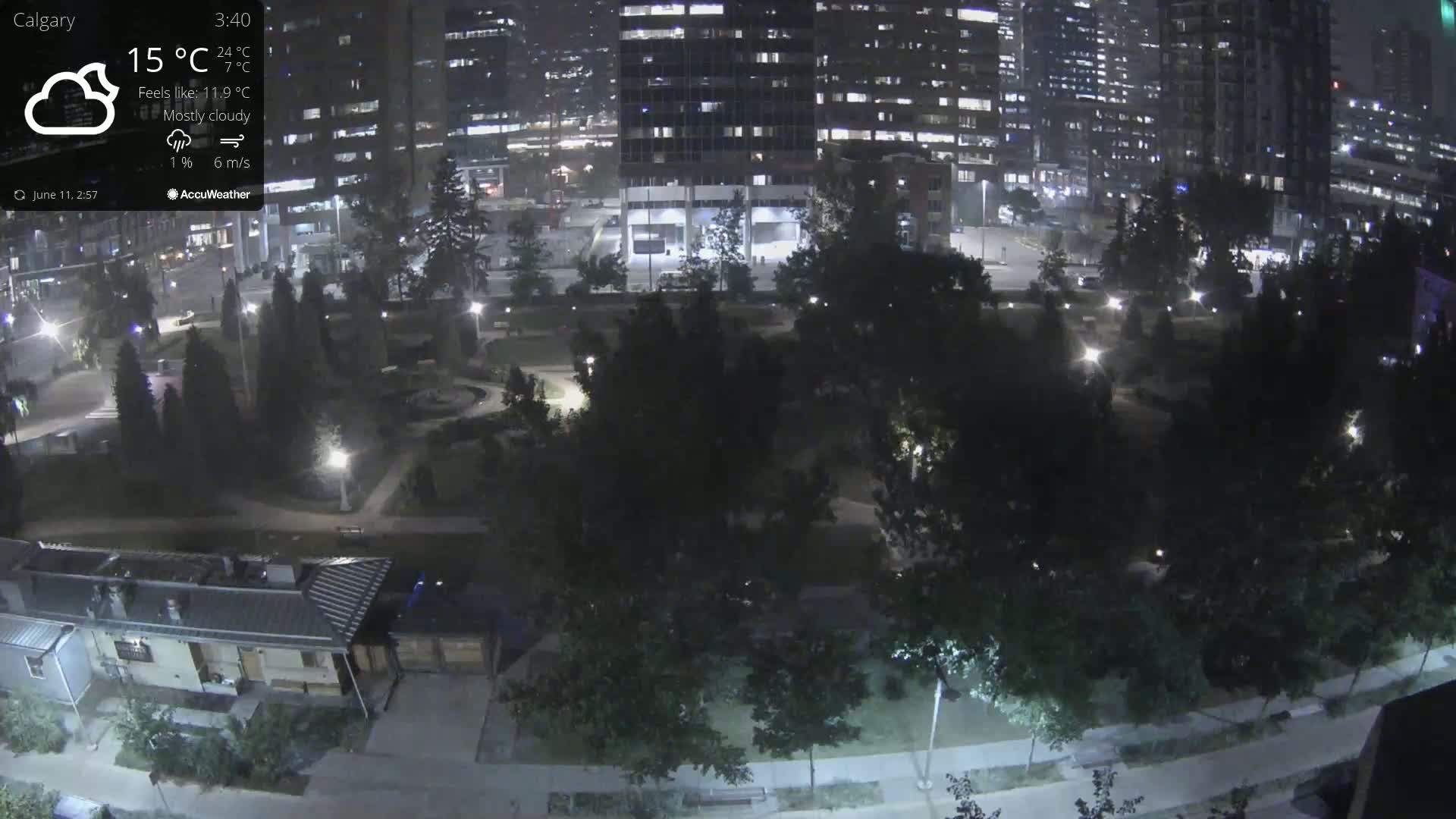 A nighttime, mostly cloudy view of a park with buildings in the background, illuminated by streetlights.