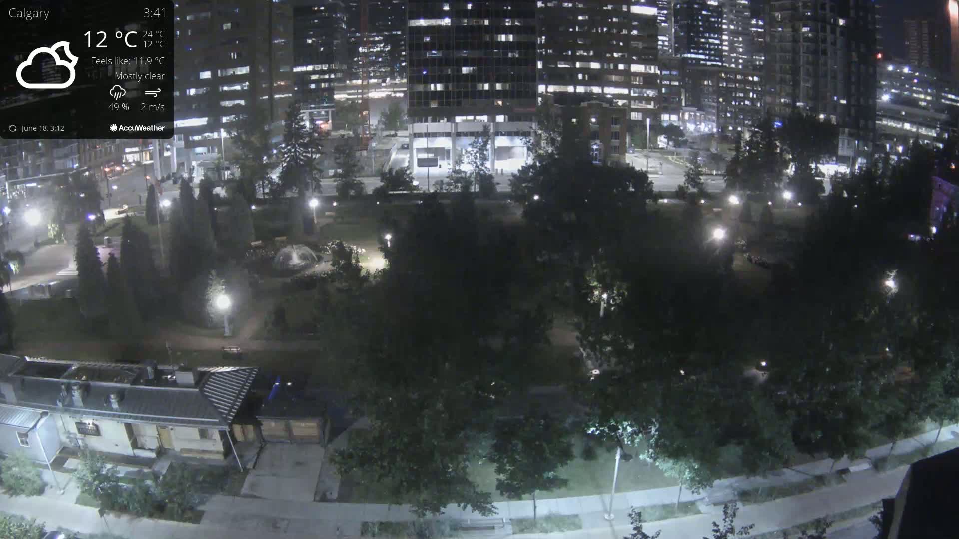 A nighttime view of a park with city buildings in the background under mostly clear skies.