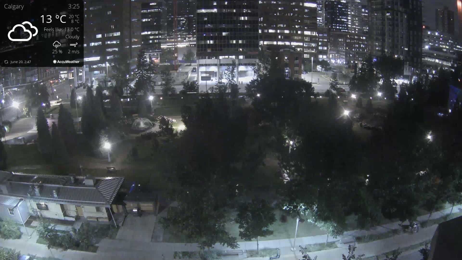 A nighttime, cloudy view of a park with trees and buildings in the background.