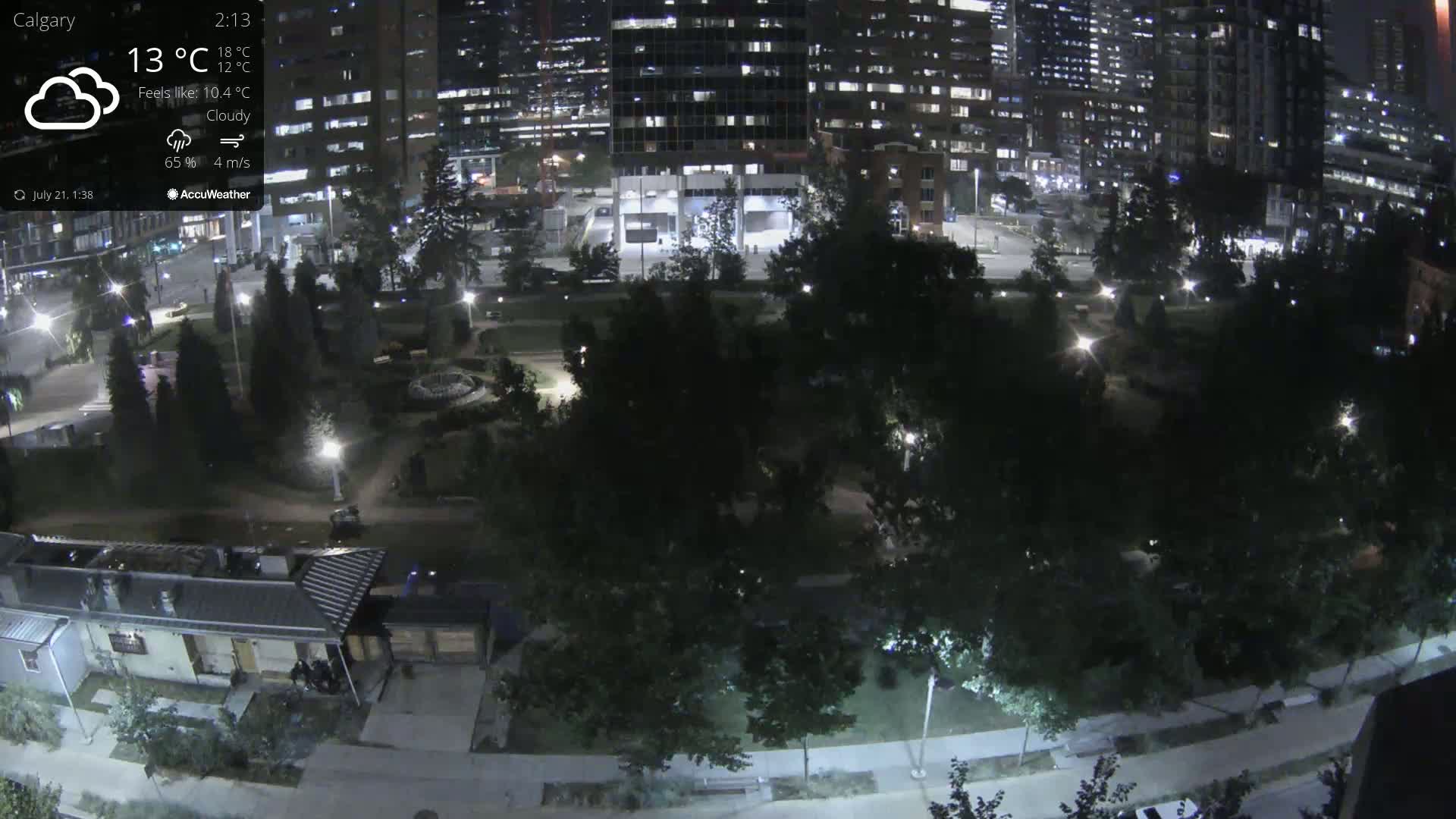 A nighttime, cloudy view of a city park surrounded by illuminated buildings and trees.